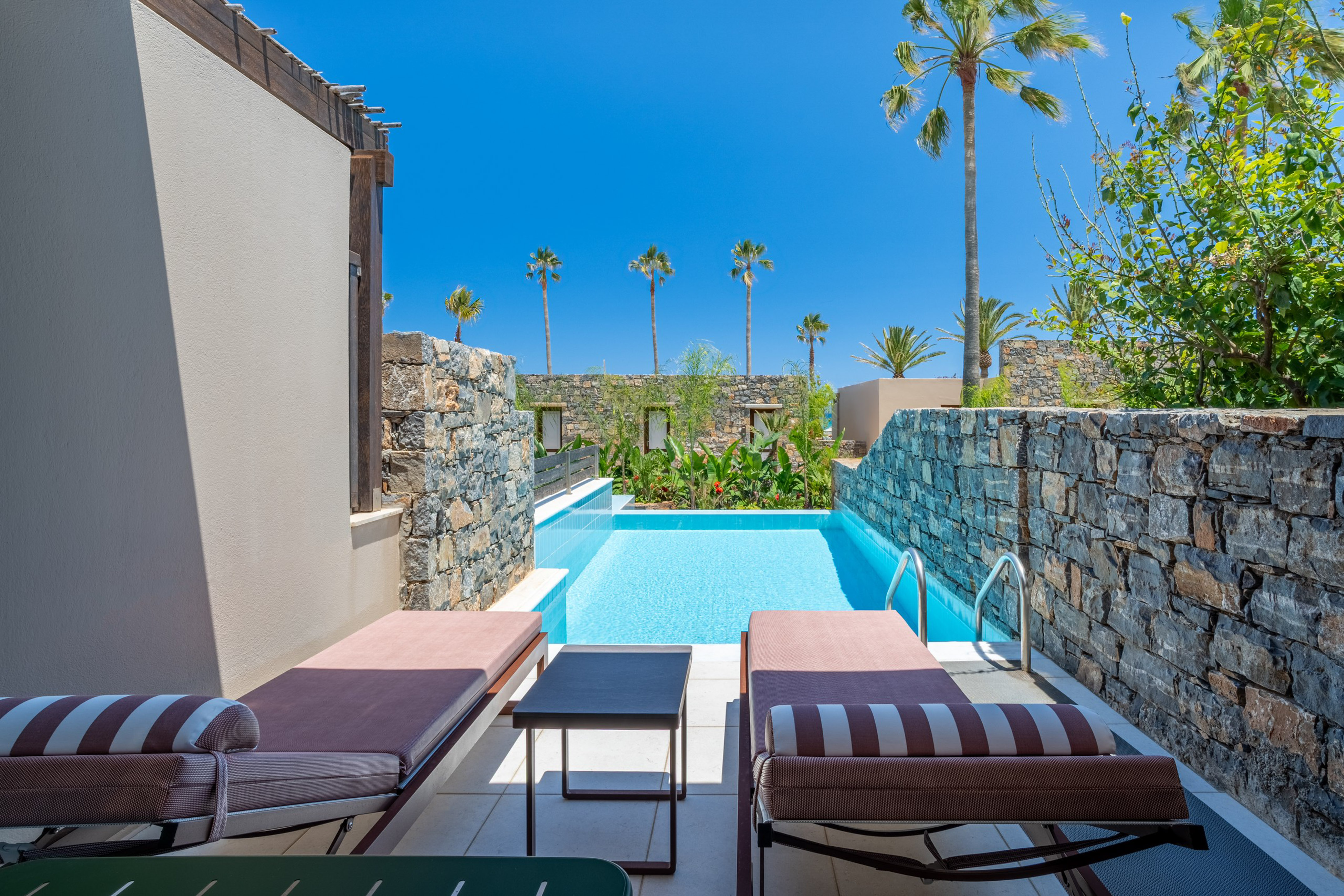 Resort private pool with sun loungers, stone walls, and palm trees.