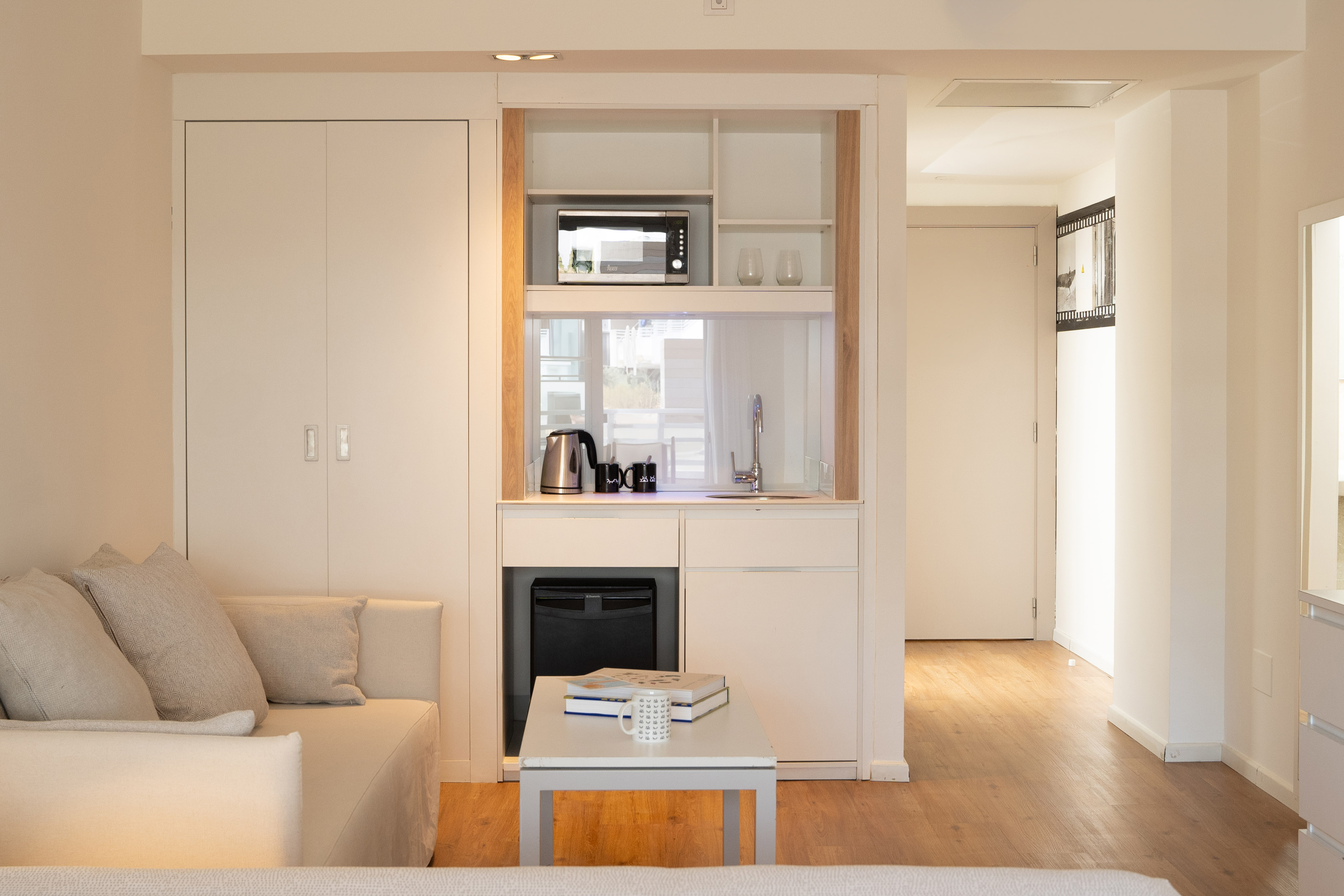 Compact modern studio with integrated kitchenette, sofa, and wood flooring.