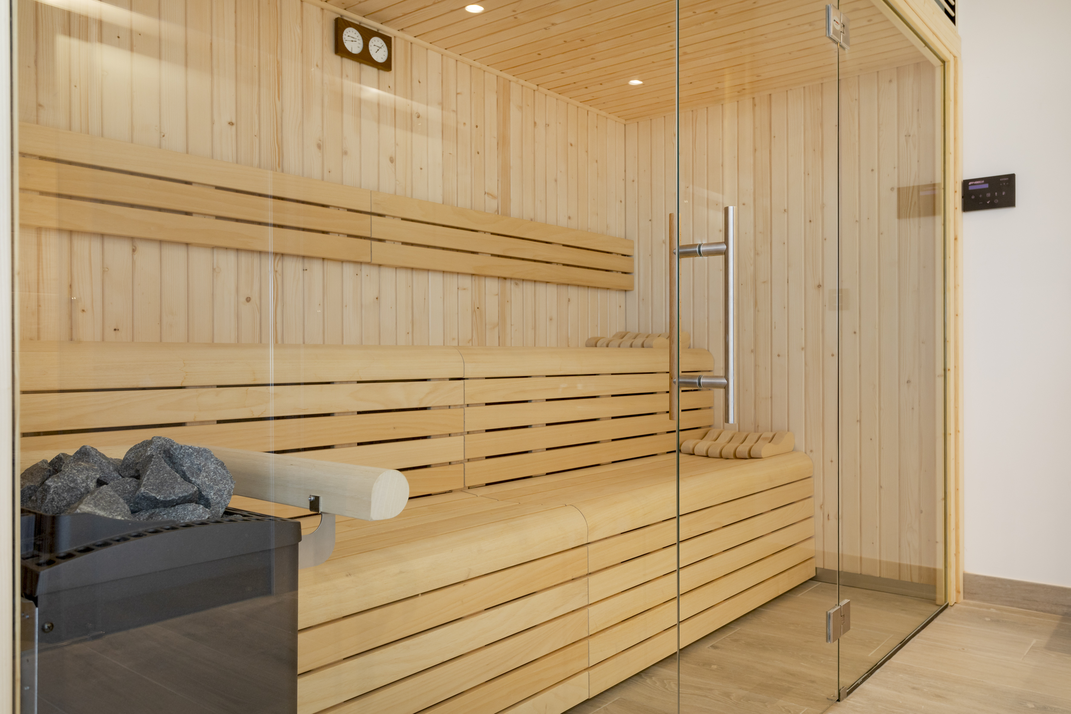 Modern wooden sauna interior with benches, heater, and glass door.