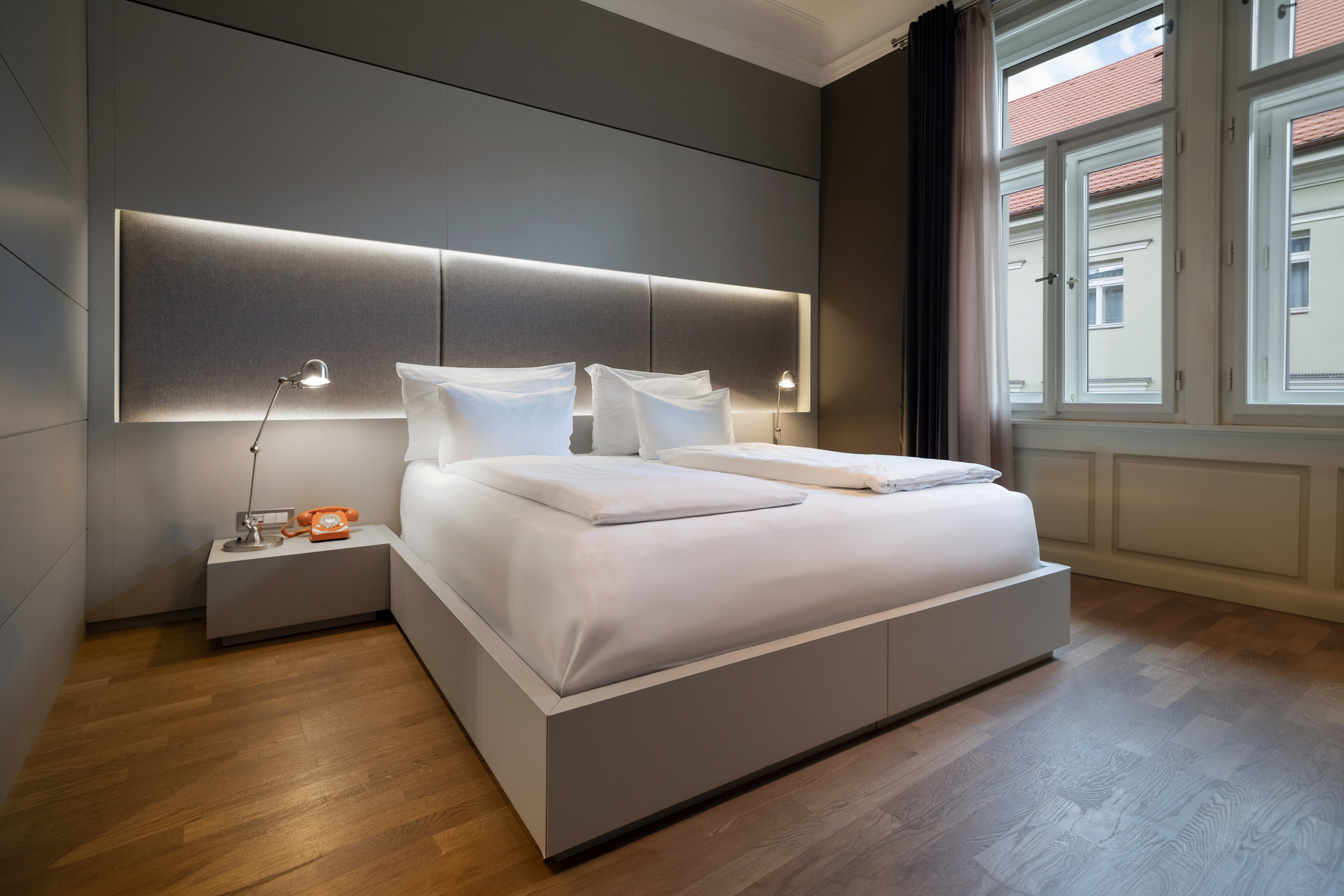 Upscale hotel room featuring a white bed, illuminated headboard, and wood flooring.