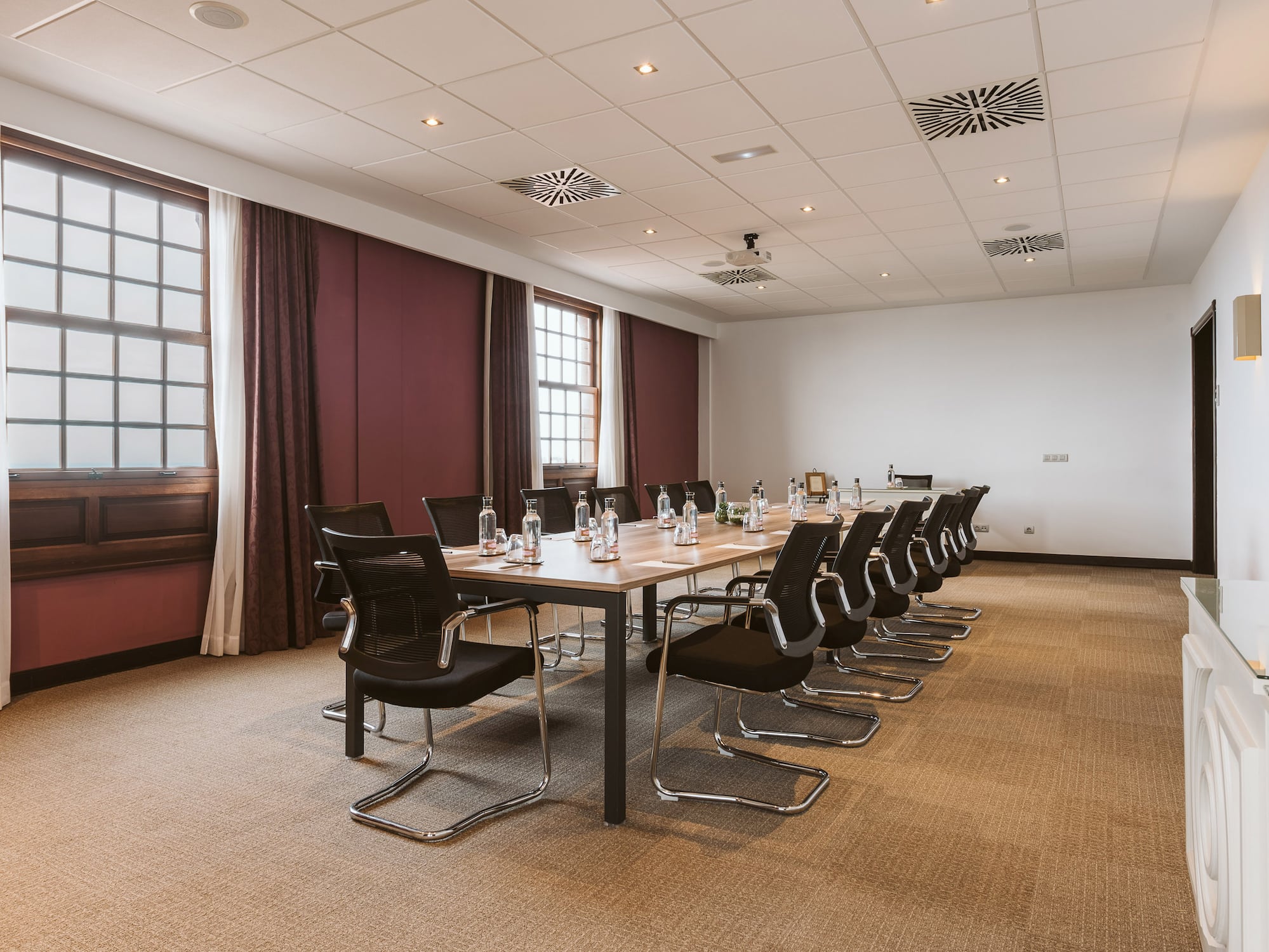 Conference room with long table, black chairs, water bottles, and tall windows.
