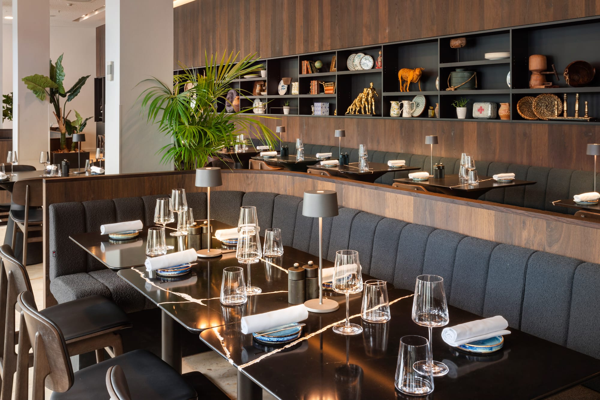 Modern restaurant dining room with marble tables, grey booths, and wall decor.