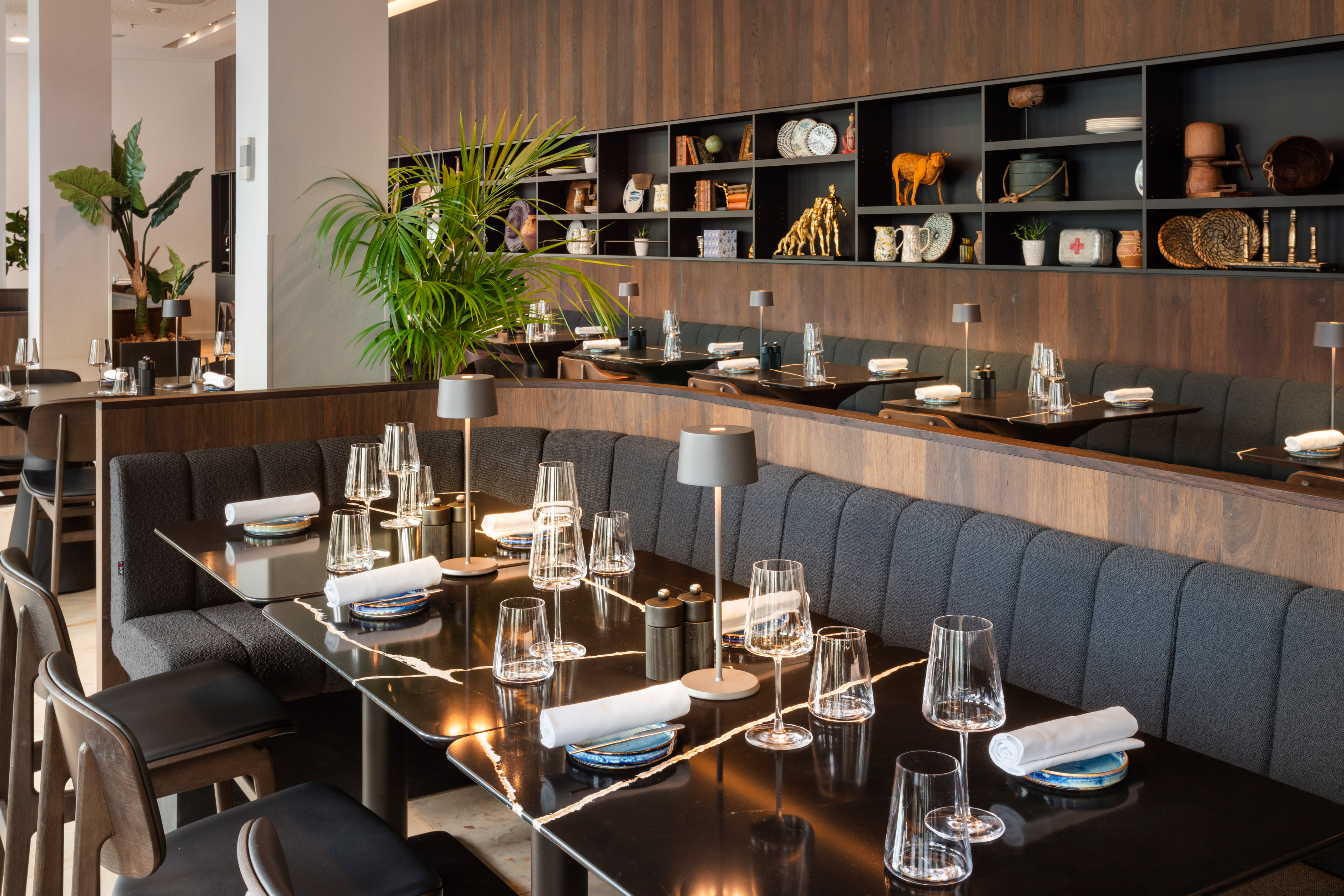 Modern restaurant dining room with marble tables, grey booths, and wall decor.