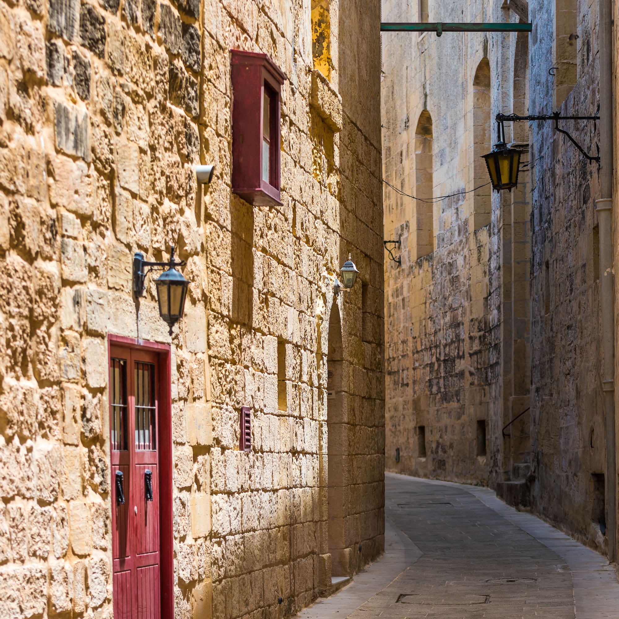 Historic stone alleyway with red door, lanterns, and textured walls.