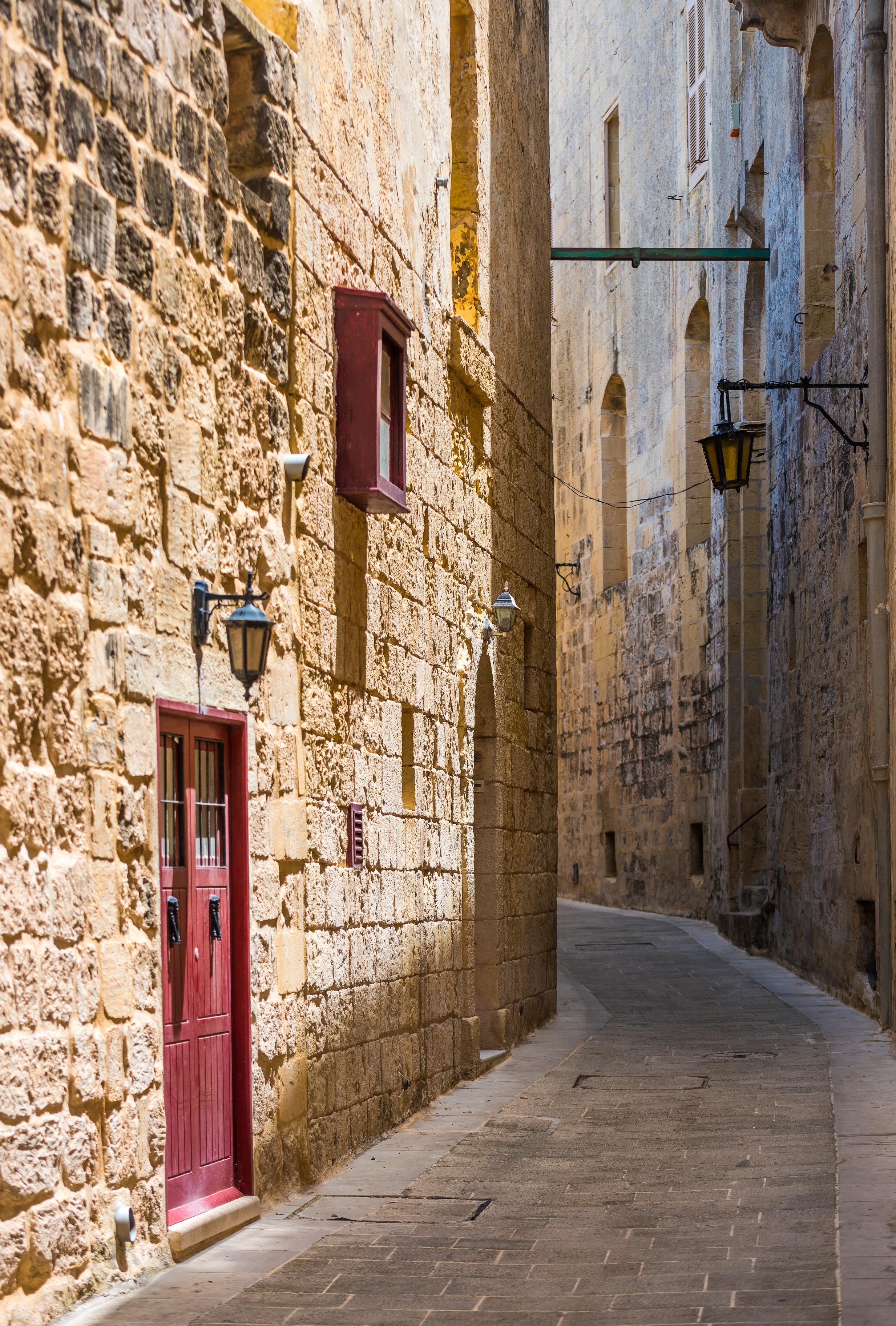 Historic stone alleyway with red door, lanterns, and textured walls.