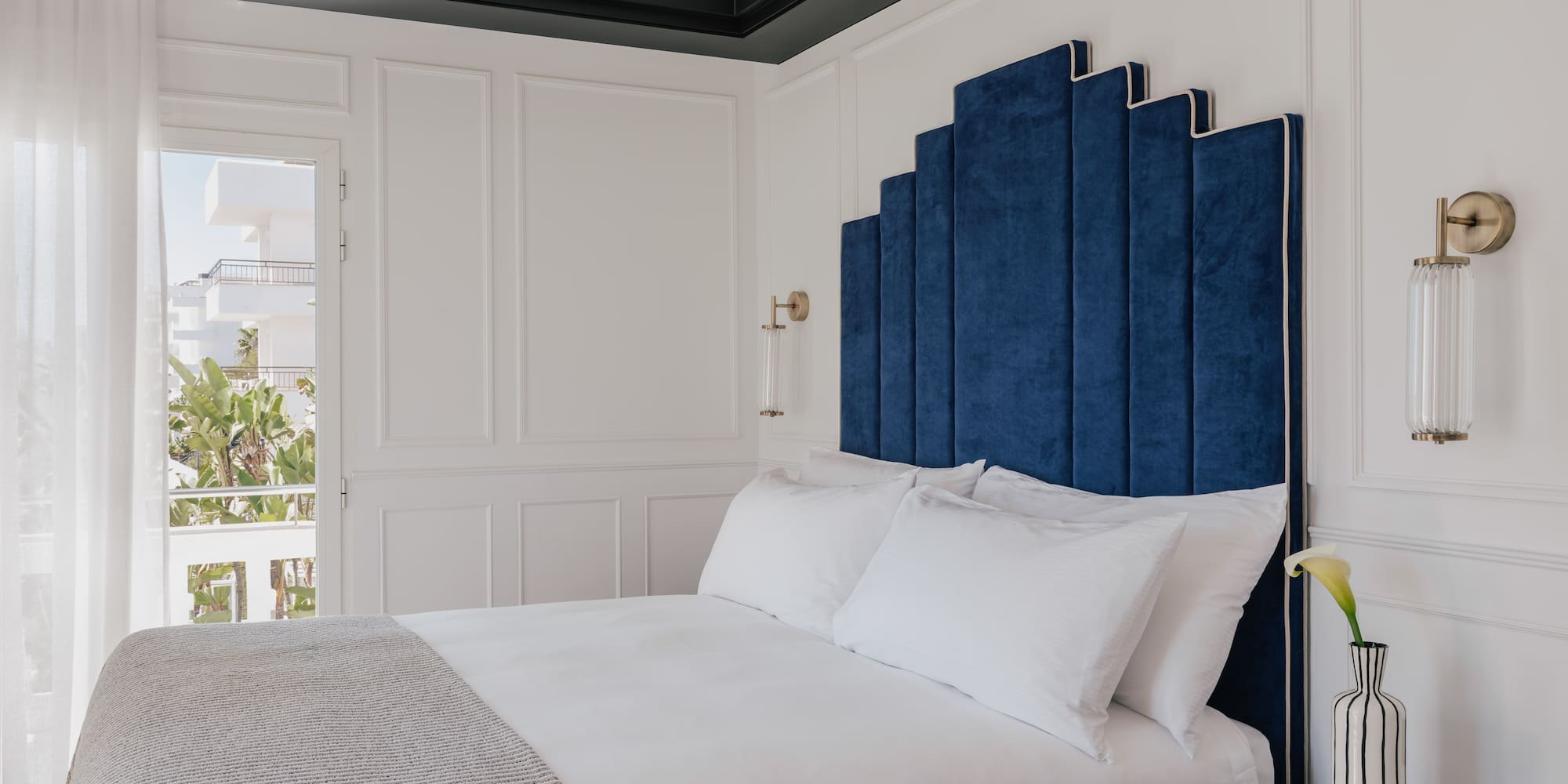 Blue velvet art deco headboard in a luxurious white hotel bedroom.