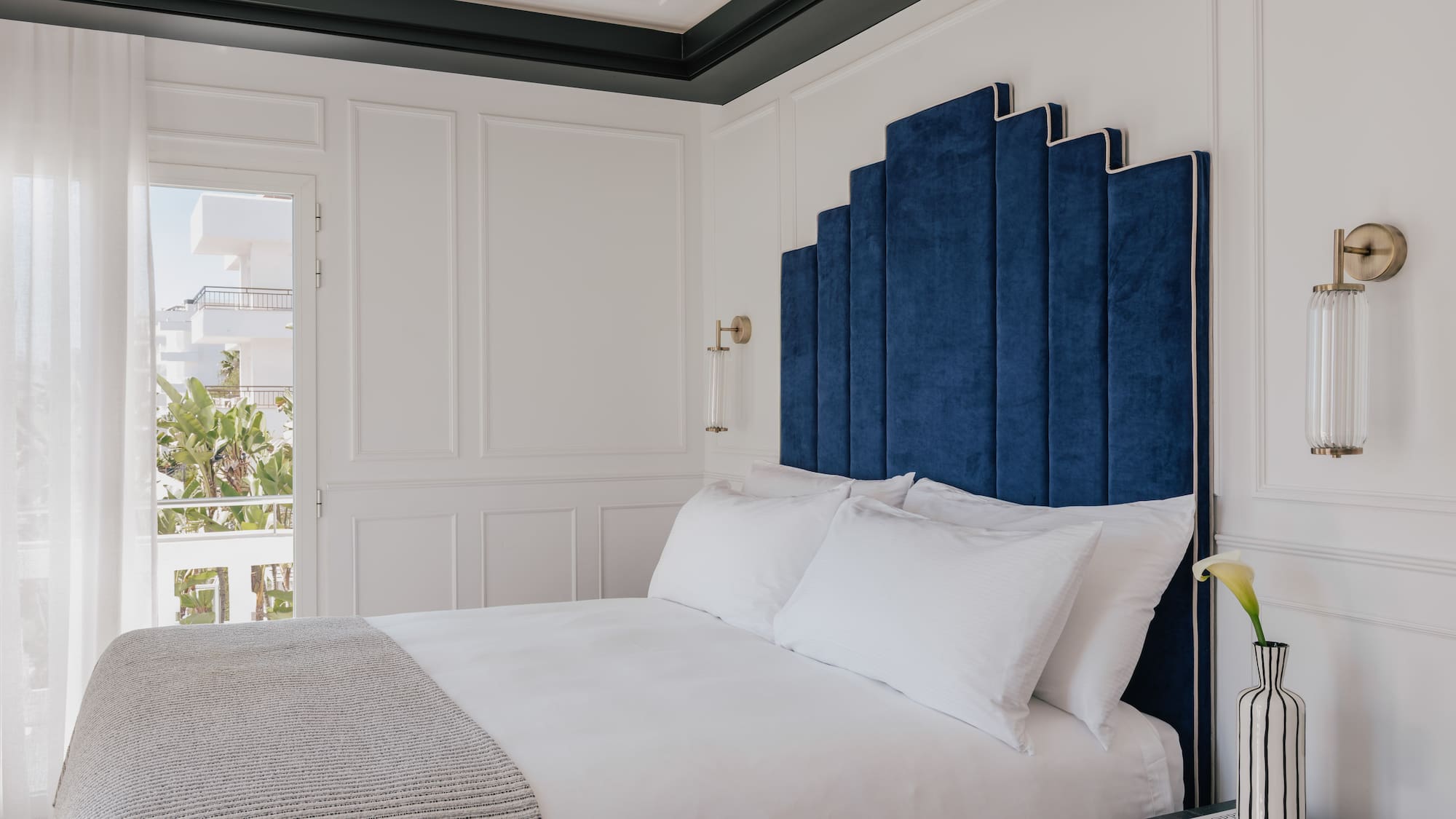 Blue velvet art deco headboard in a luxurious white hotel bedroom.