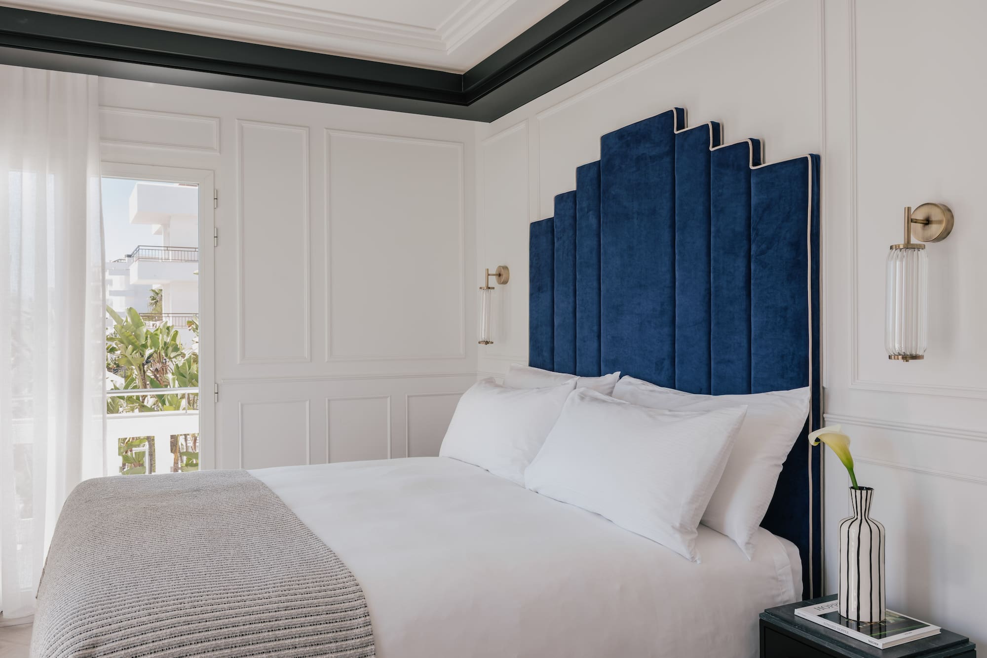 Blue velvet art deco headboard in a luxurious white hotel bedroom.