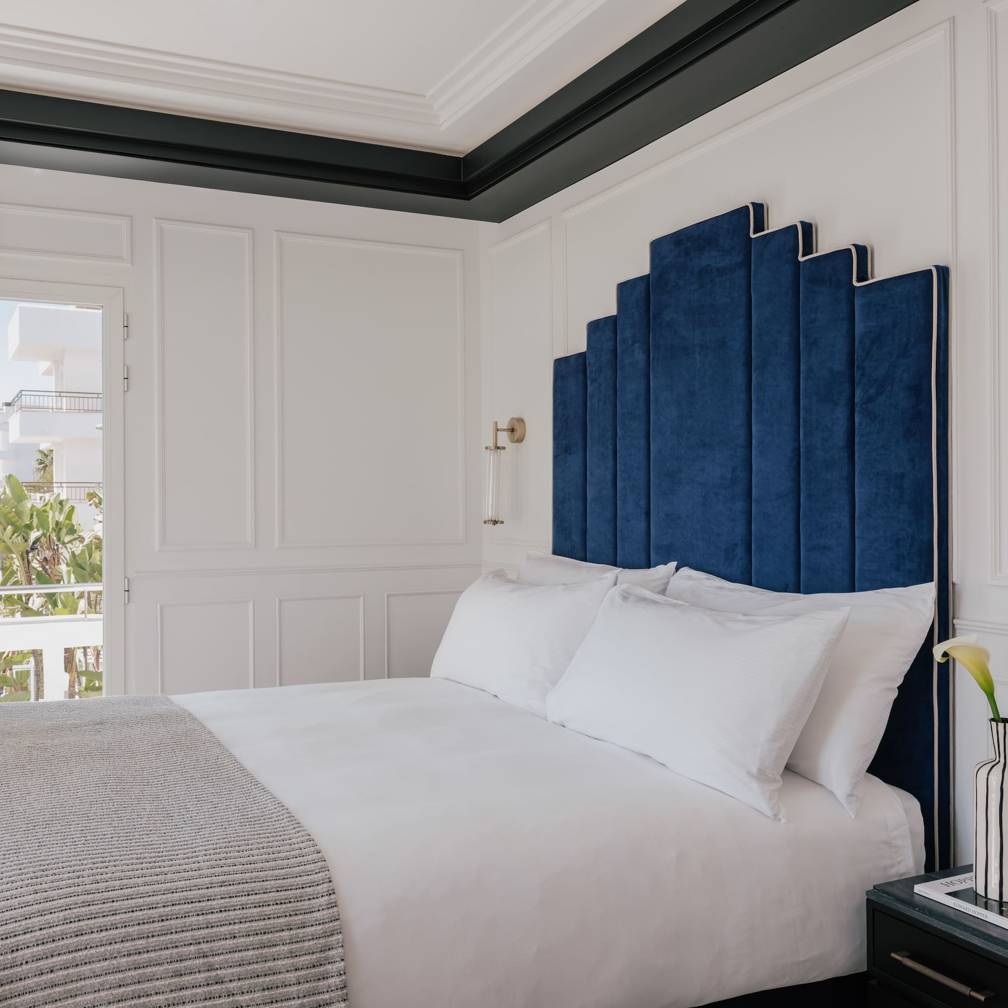 Blue velvet art deco headboard in a luxurious white hotel bedroom.