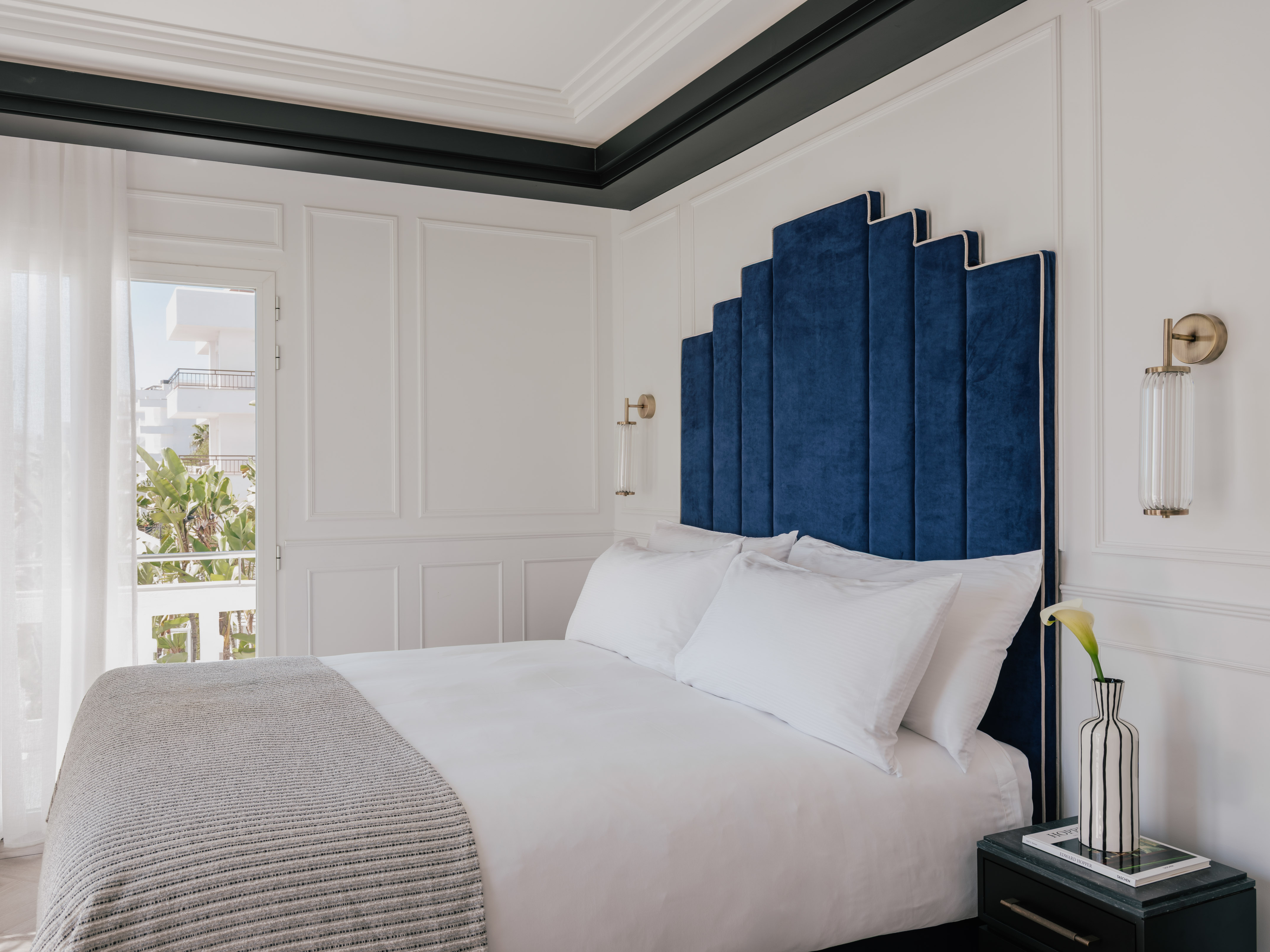 Blue velvet art deco headboard in a luxurious white hotel bedroom.