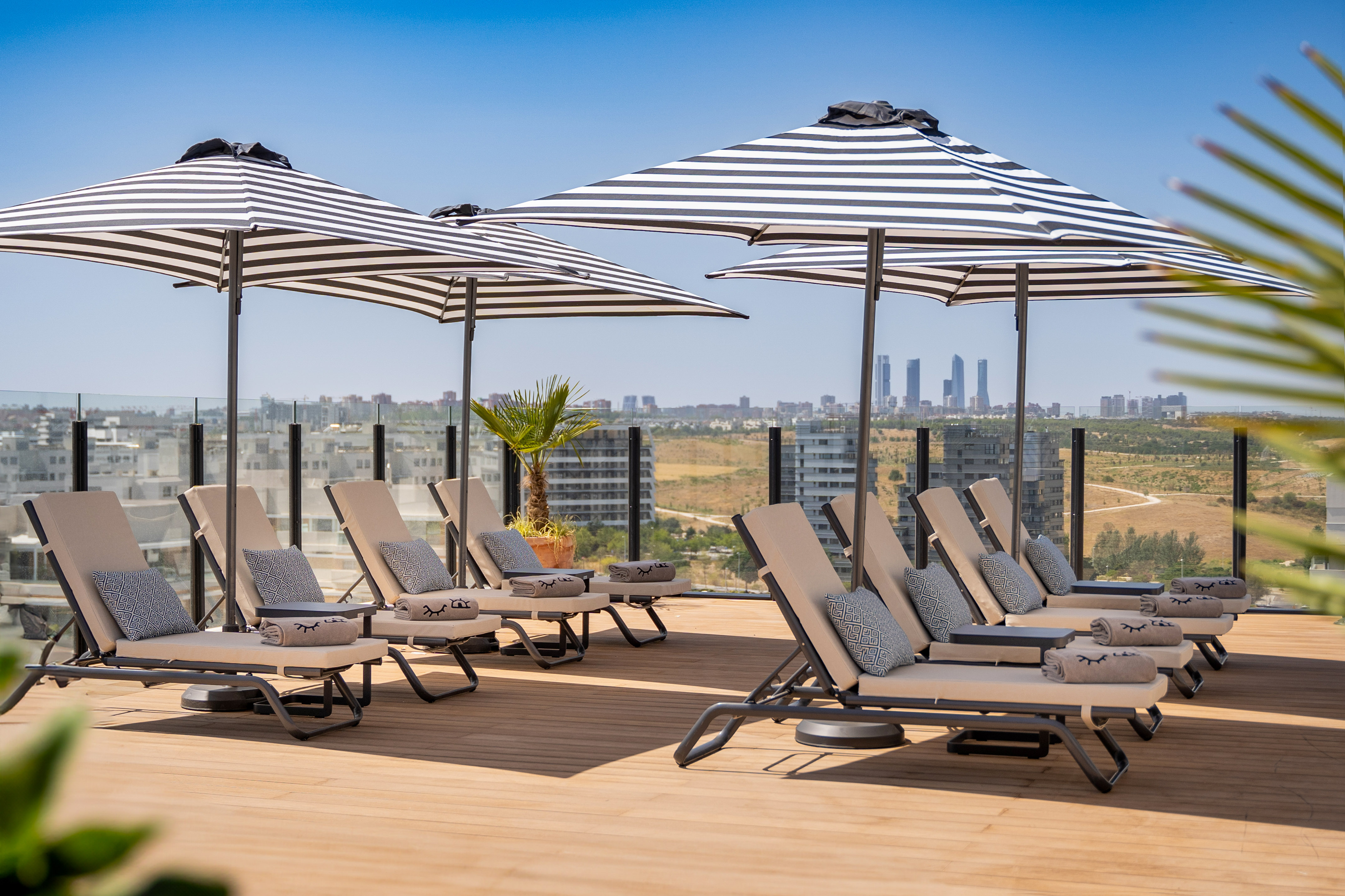 Rooftop lounge with striped umbrellas, deck chairs, and Madrid city skyline.