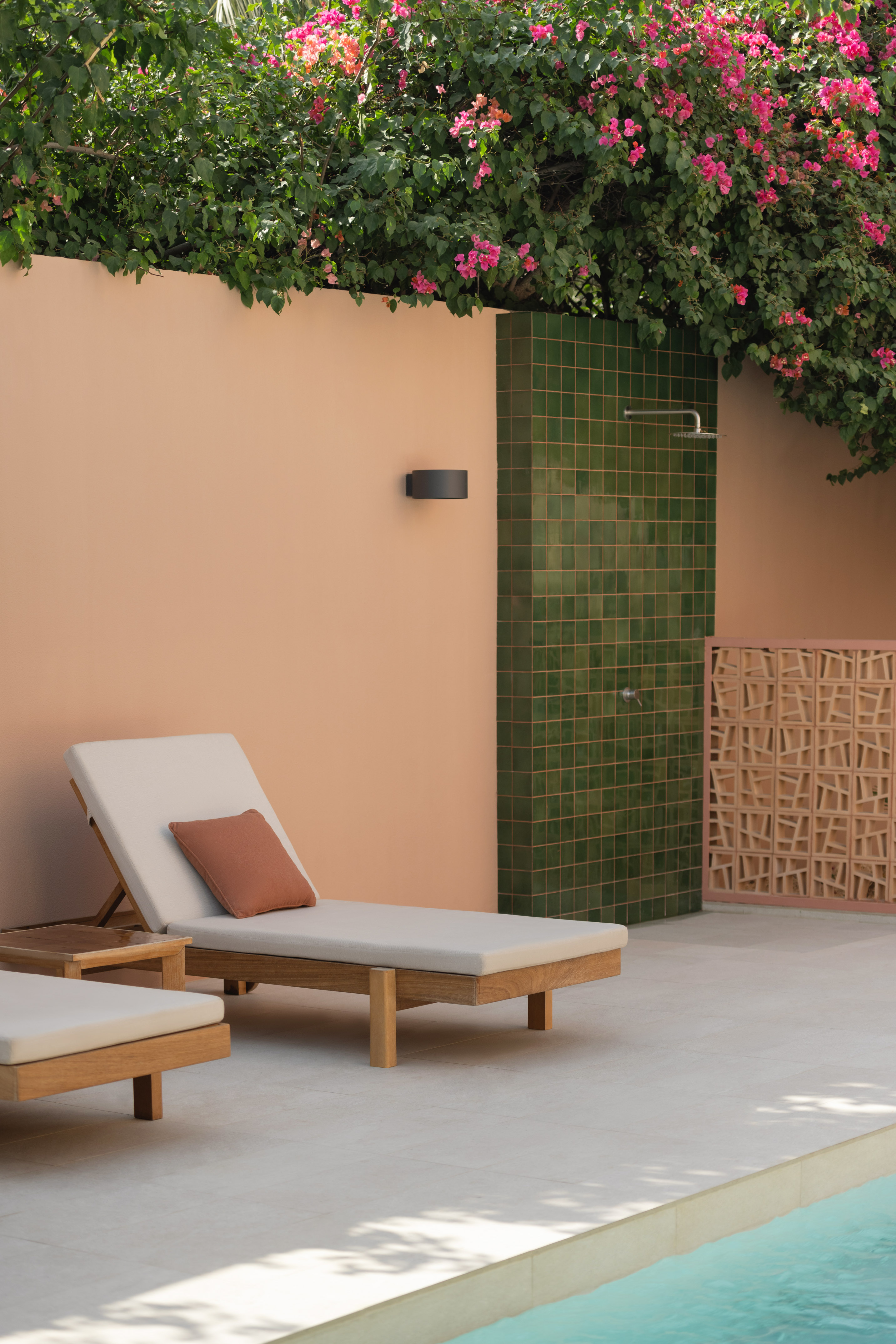 Modern patio with wooden sun loungers, outdoor shower, vibrant bougainvillea, and pool.