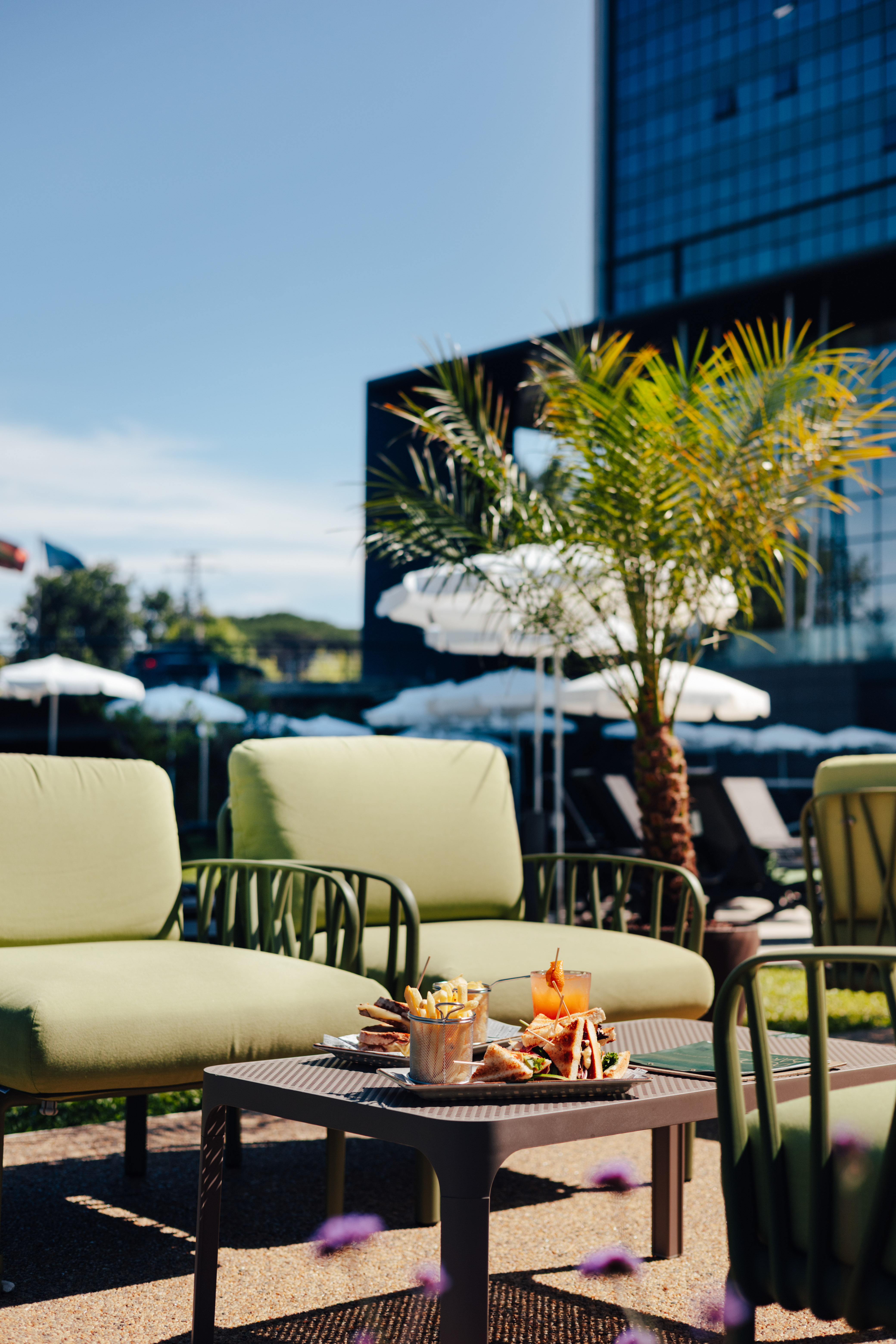 Sunny resort patio with club sandwiches, fries, cocktail, green lounge chairs.