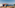 Multi-level oceanfront restaurant with wooden decks, glass walls, outdoor dining, and blue sky.