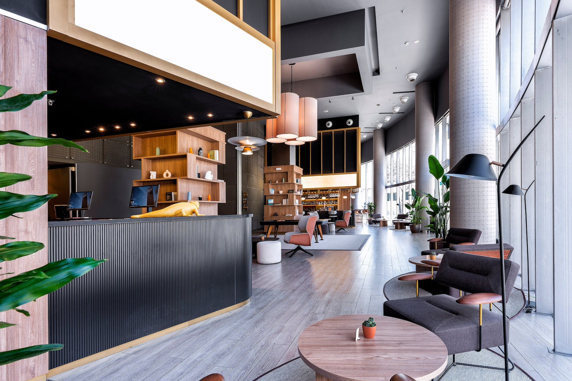 Modern hotel lobby: reception desk, lounge seating, natural light, bar area.