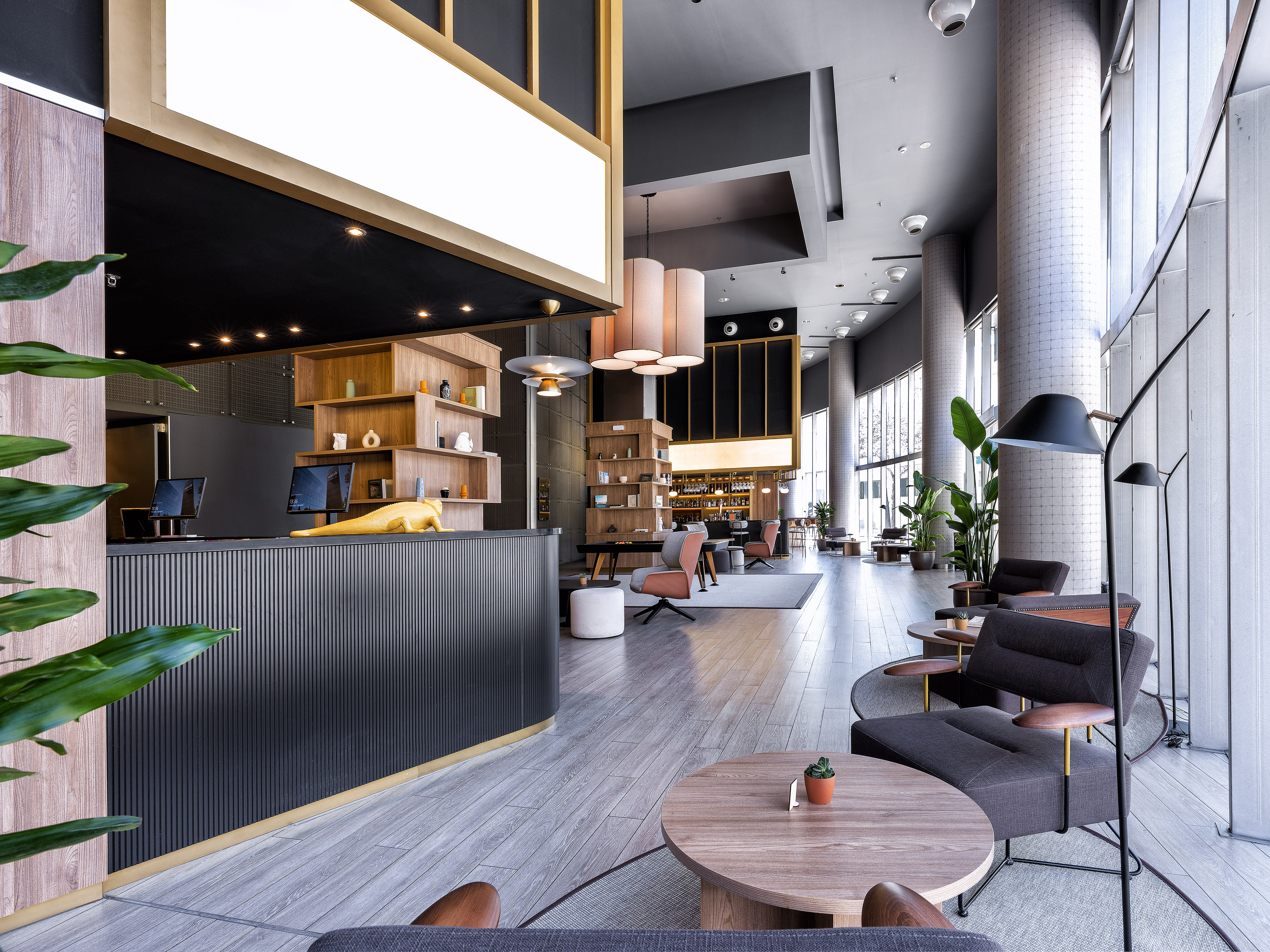 Modern hotel lobby: reception desk, lounge seating, natural light, bar area.