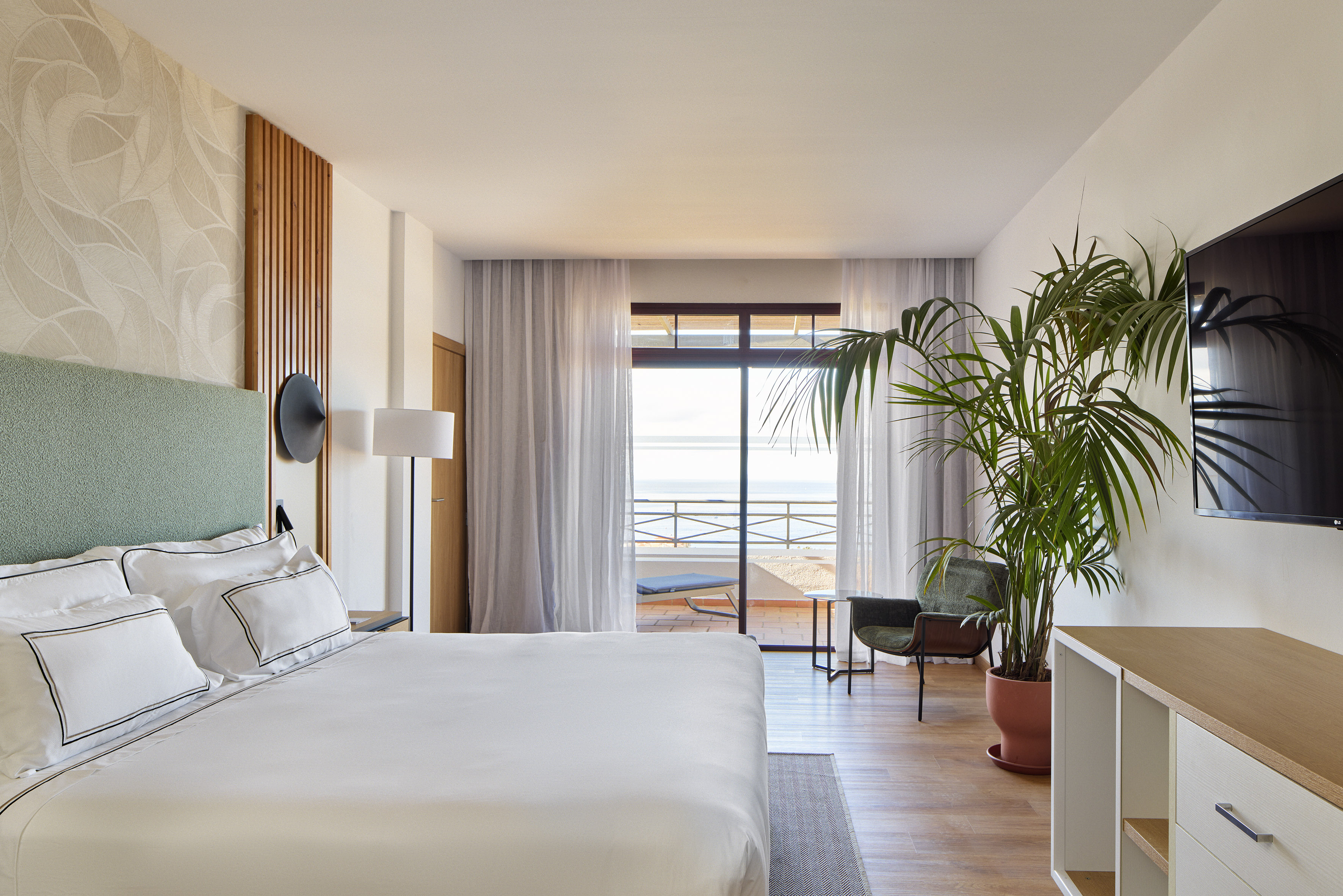 Bright hotel room with ocean view balcony, white bed, modern decor.