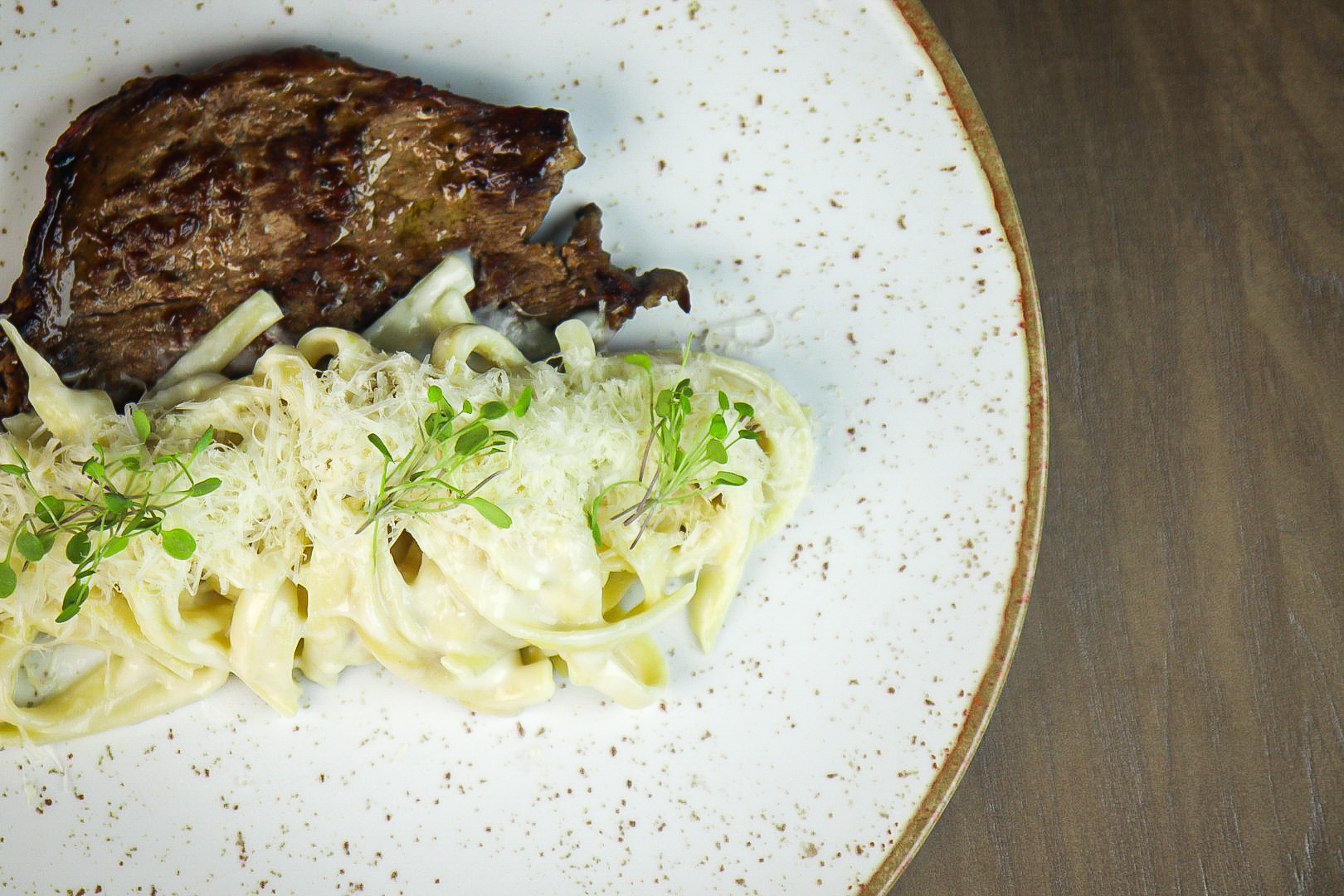 Steak and creamy fettuccine pasta with parmesan and microgreens.