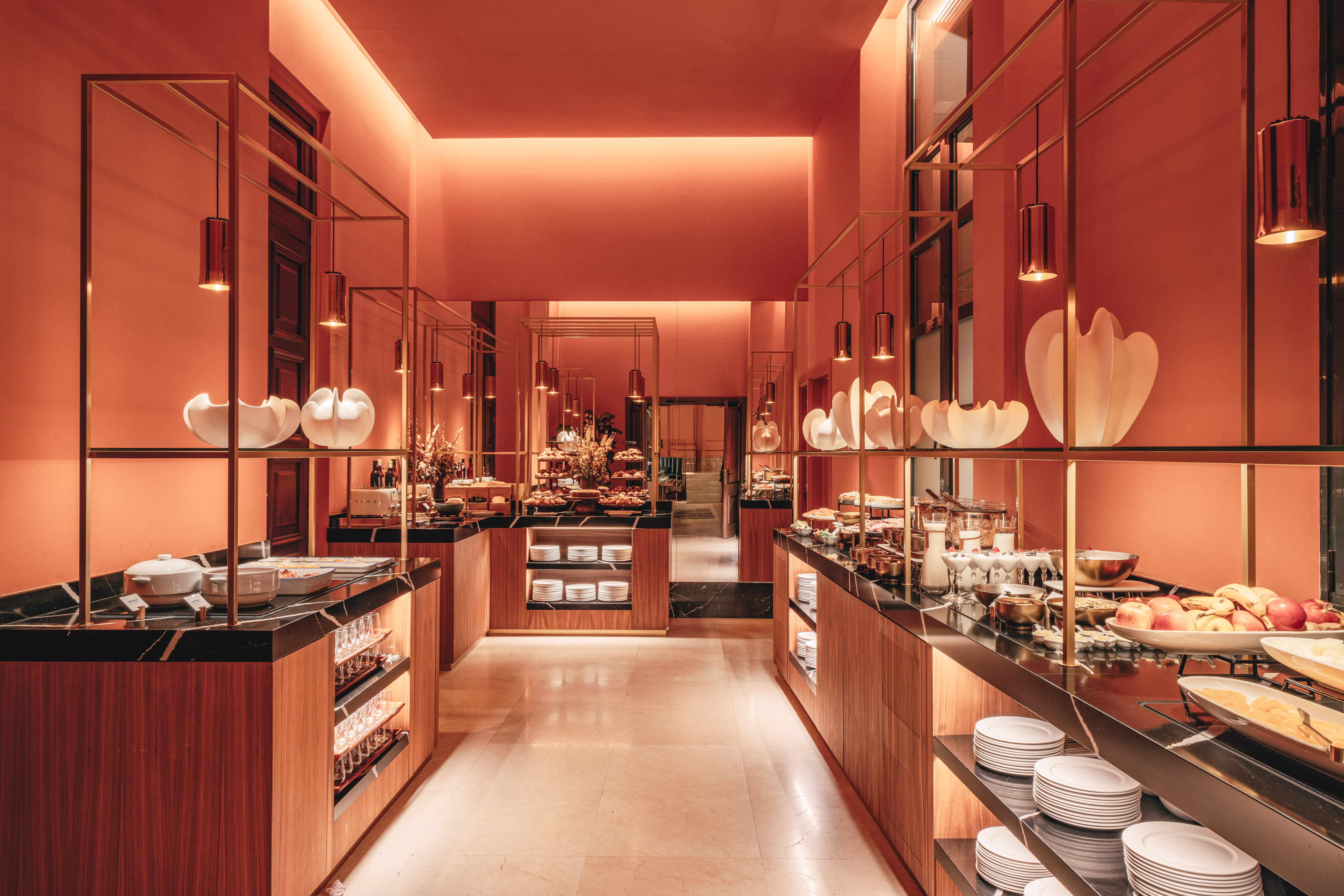 Modern coral buffet with gold framework, marble counters, and food offerings.