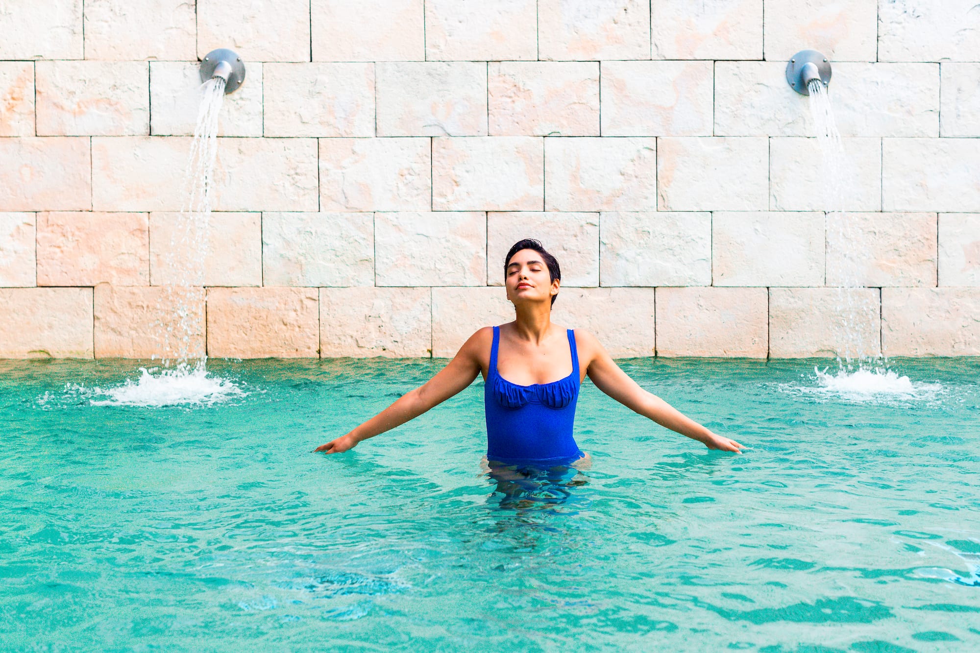 a woman in a blue swimsuit in a pool with water jets