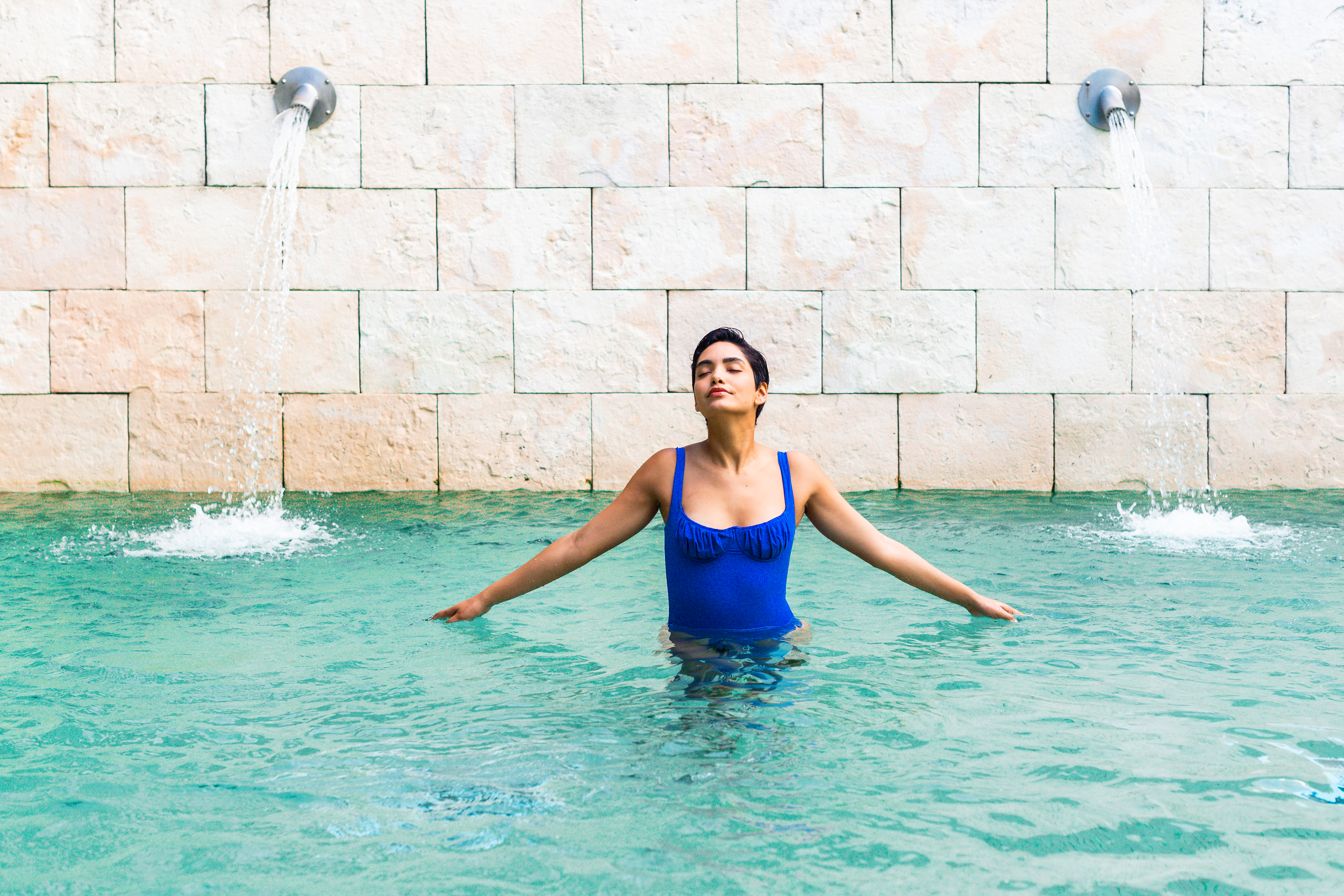 a woman in a blue swimsuit in a pool with water jets
