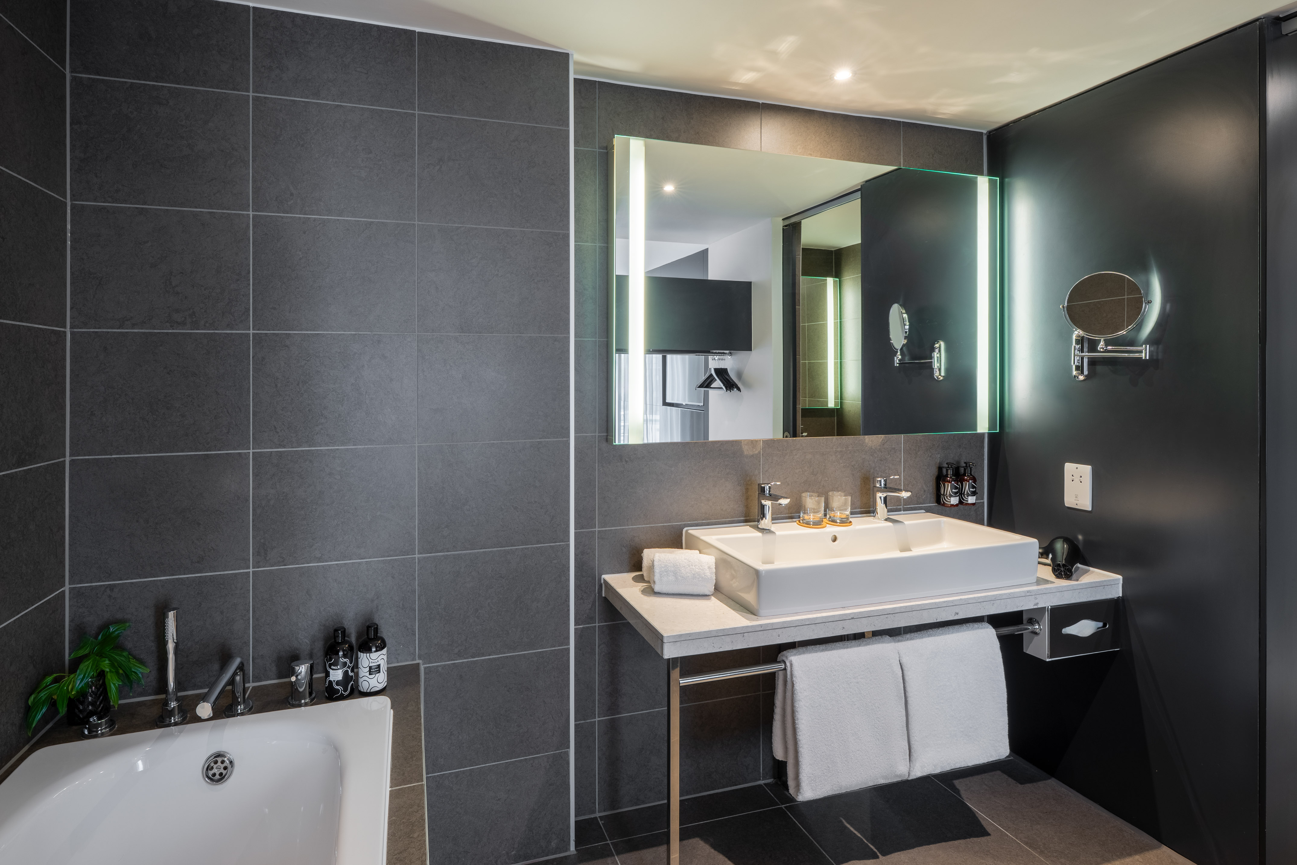 Modern gray bathroom with white sink, tub, chrome fixtures, and illuminated mirror.
