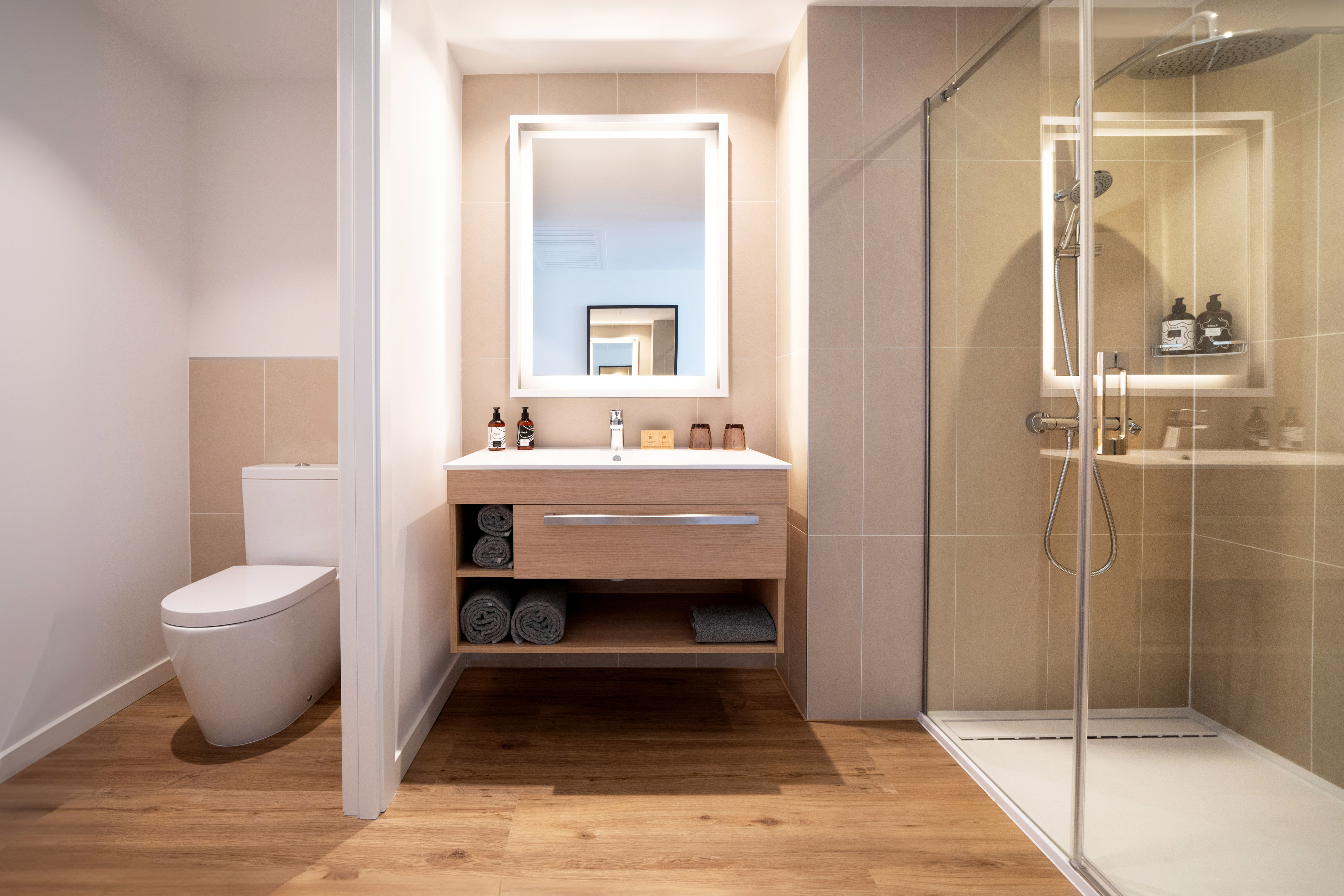 Modern bathroom with wood vanity, lighted mirror, walk-in shower, and toilet.