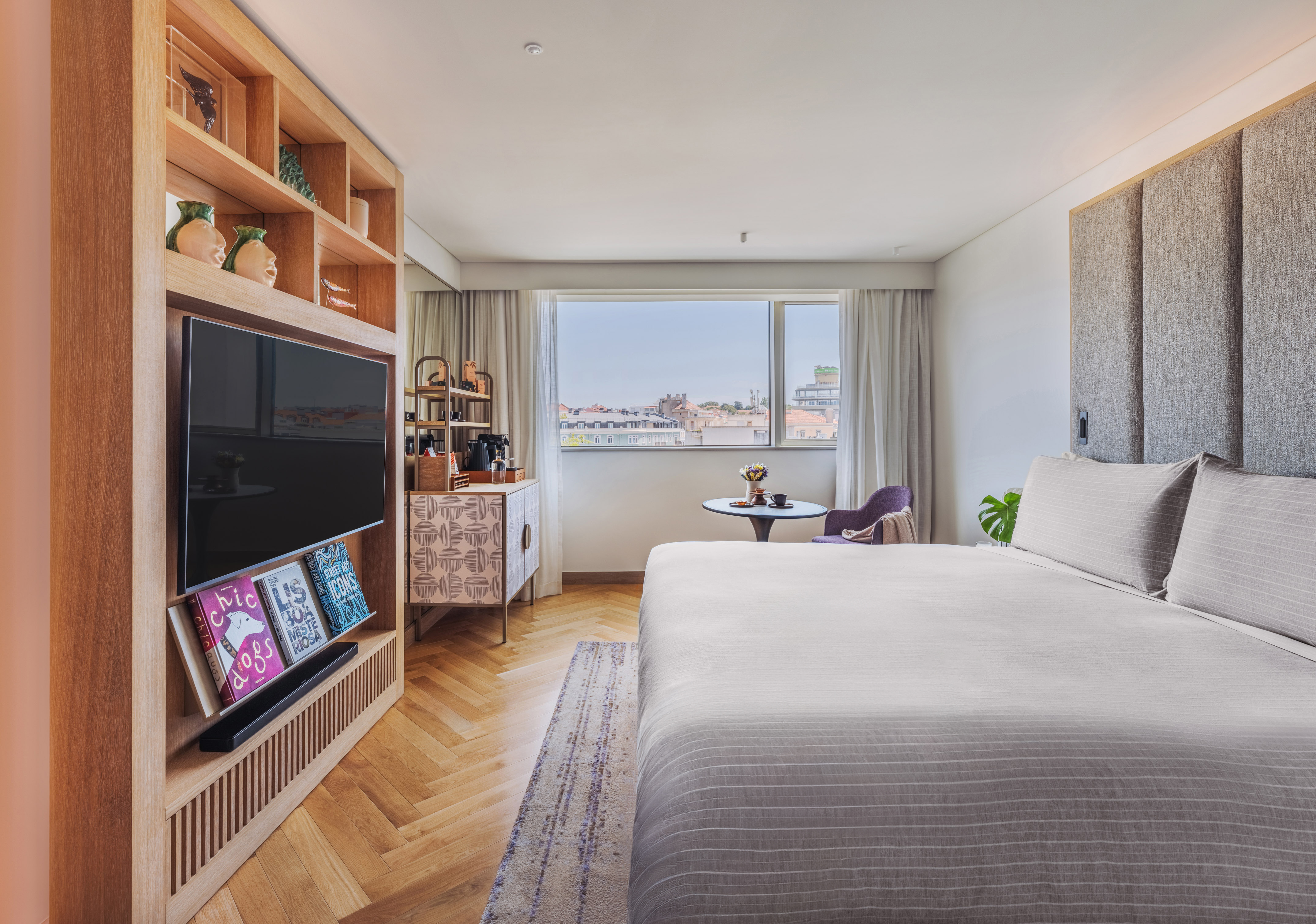 Modern hotel bedroom with city view, large bed, and built-in wooden shelving.