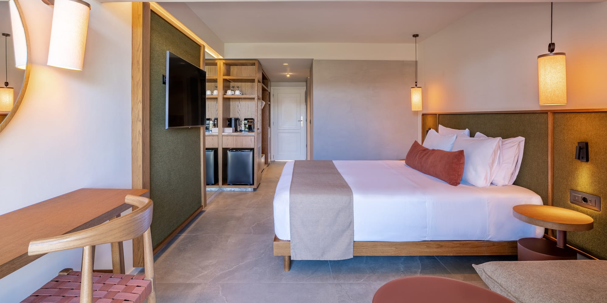 Contemporary hotel room with king bed, desk, TV, and refreshment station.