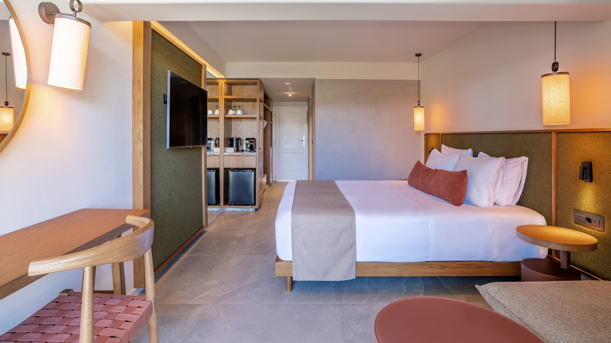 Contemporary hotel room with king bed, desk, TV, and refreshment station.