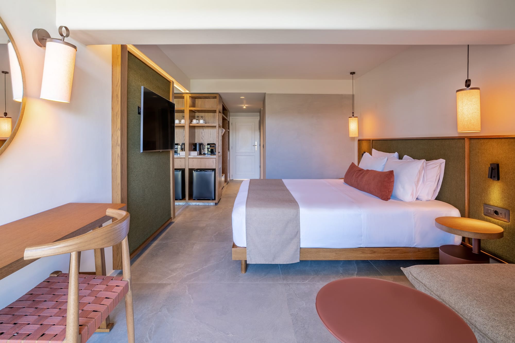 Contemporary hotel room with king bed, desk, TV, and refreshment station.