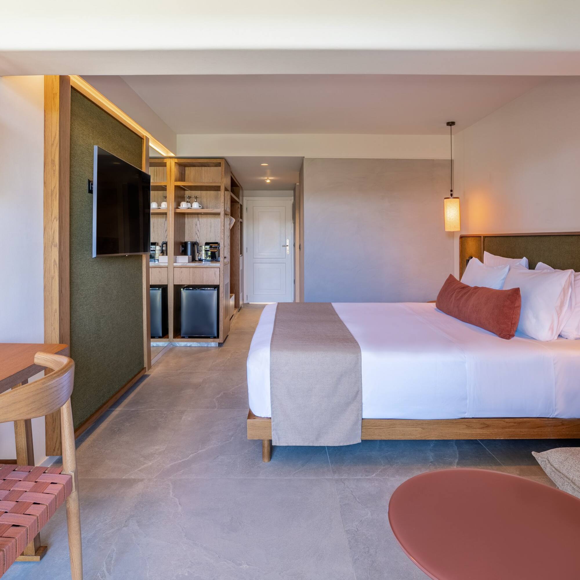 Contemporary hotel room with king bed, desk, TV, and refreshment station.