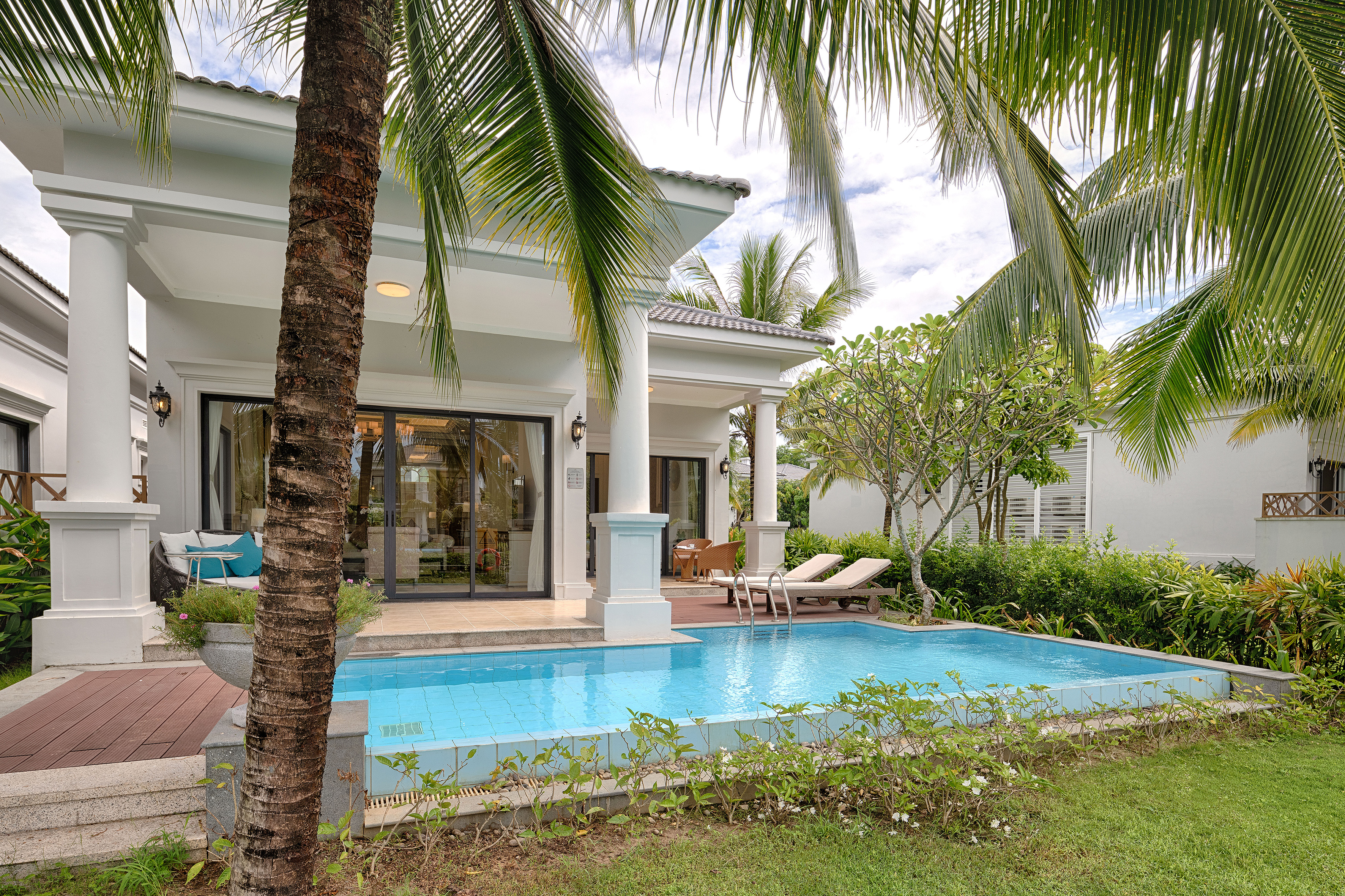 Luxury tropical villa with private pool, lounge chairs, and palm trees.