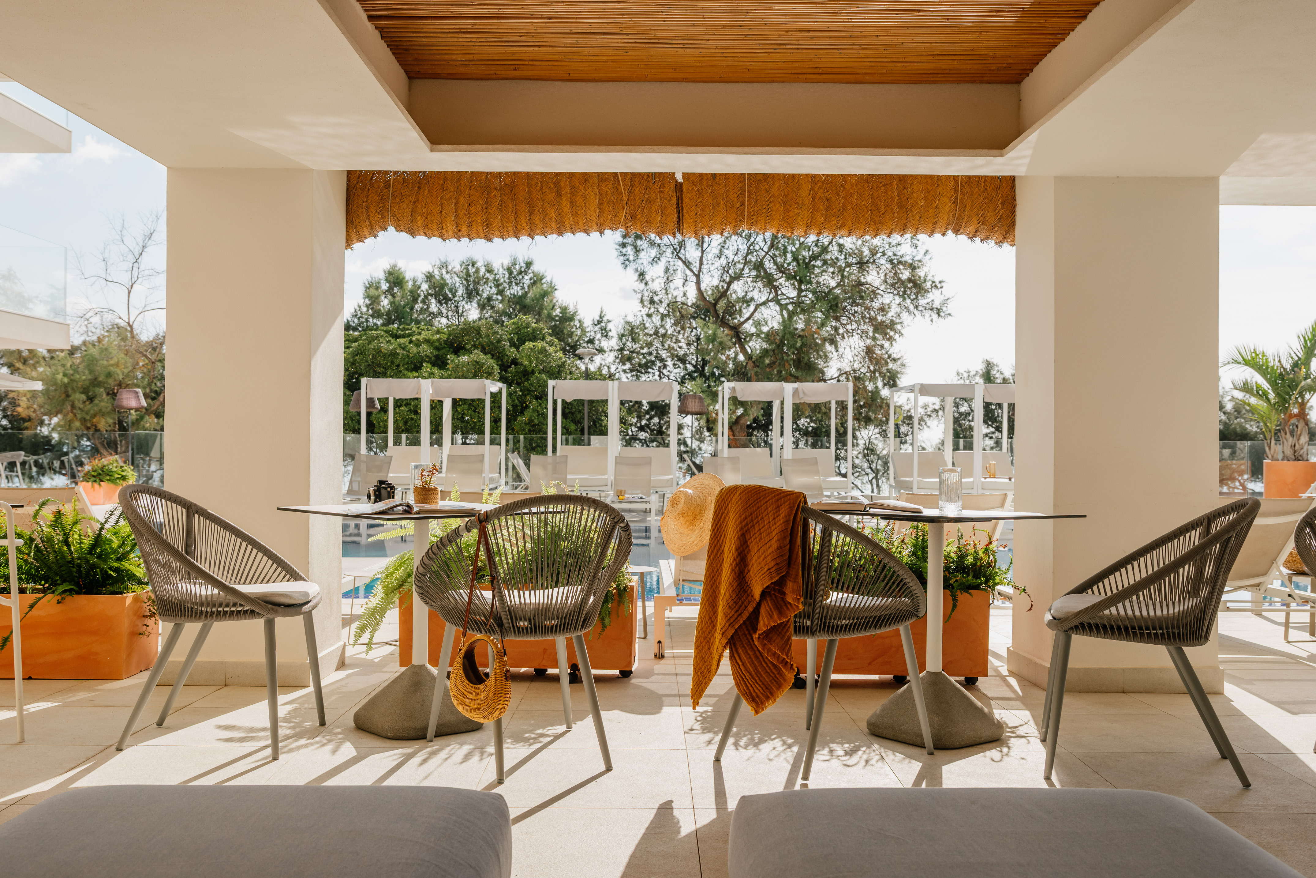 Modern outdoor patio with rope chairs, thatched ceiling, and resort pool view.