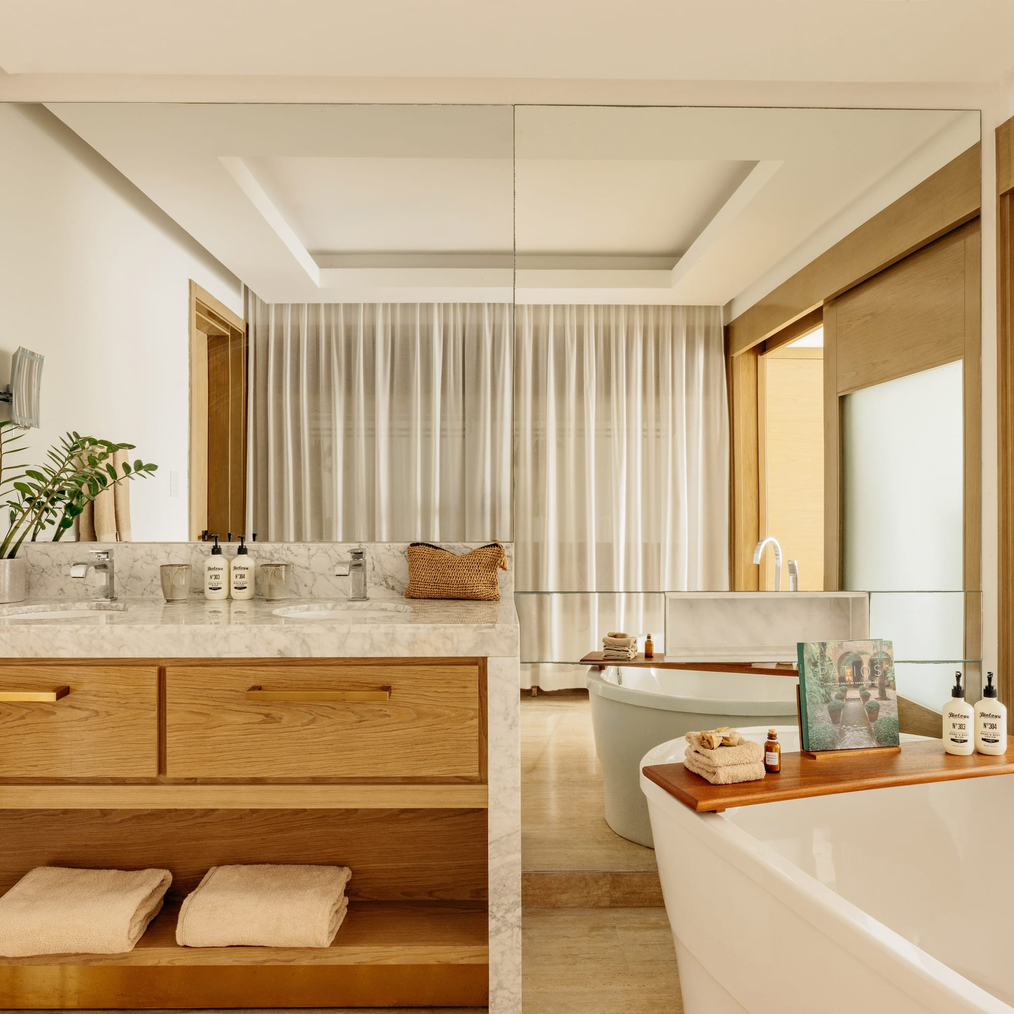 Modern bathroom featuring marble double vanity, wood cabinets, and freestanding tub.