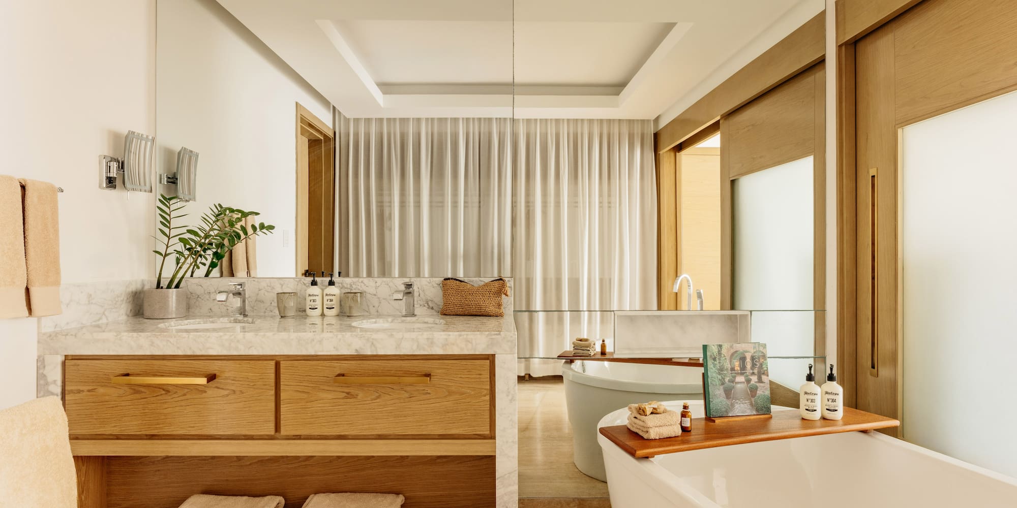 Modern bathroom featuring marble double vanity, wood cabinets, and freestanding tub.