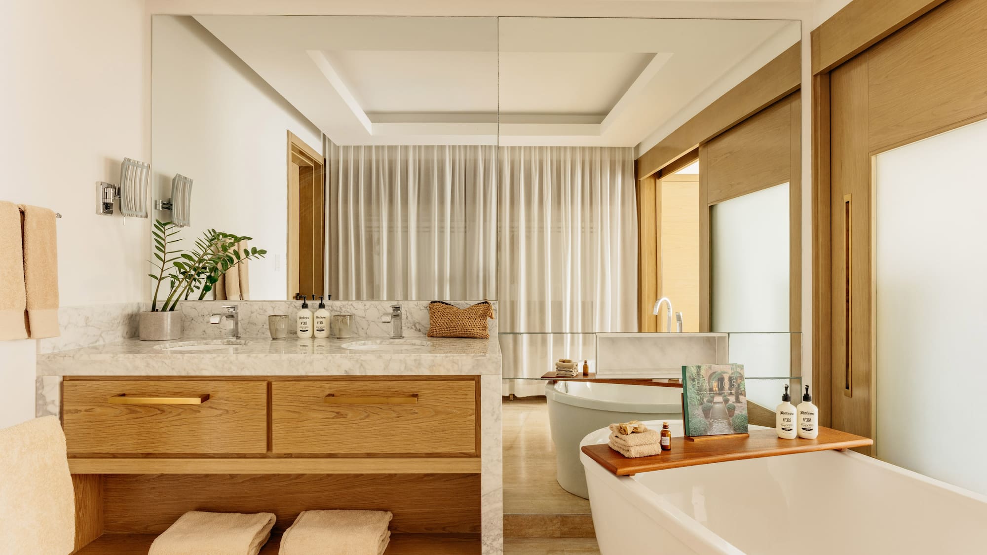 Modern spa bathroom with marble vanity, wood cabinets, and freestanding tub.