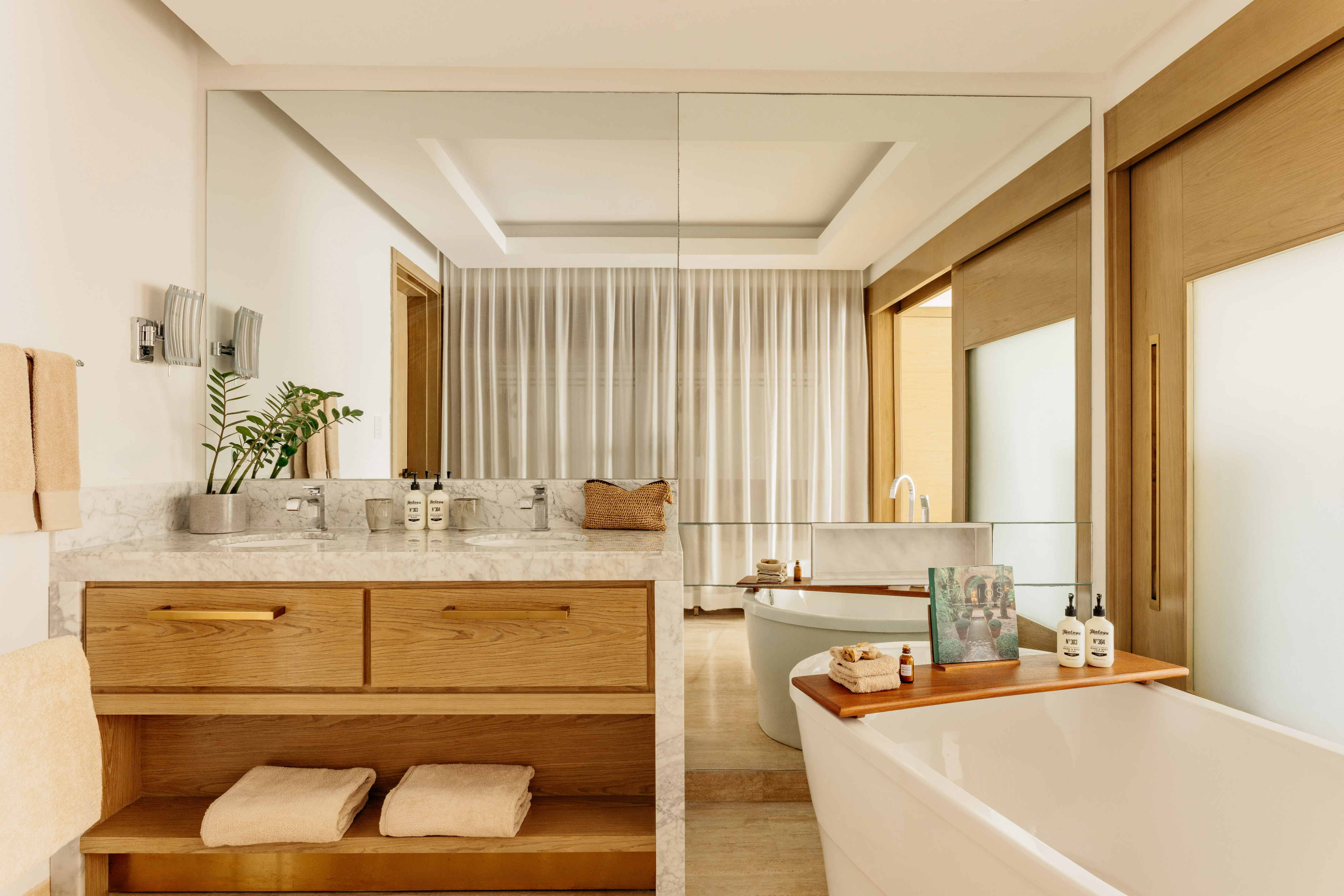 Modern bathroom featuring marble double vanity, wood cabinets, and freestanding tub.