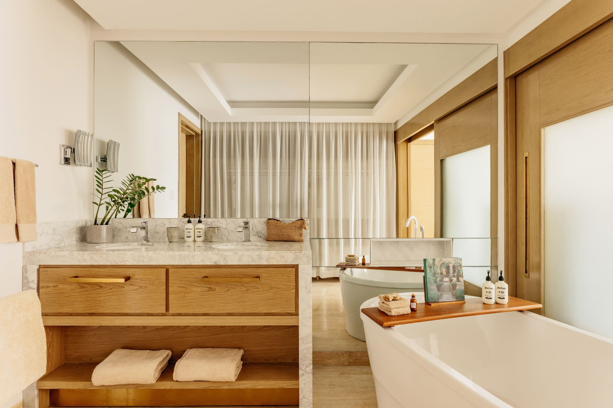 Modern bathroom featuring marble double vanity, wood cabinets, and freestanding tub.