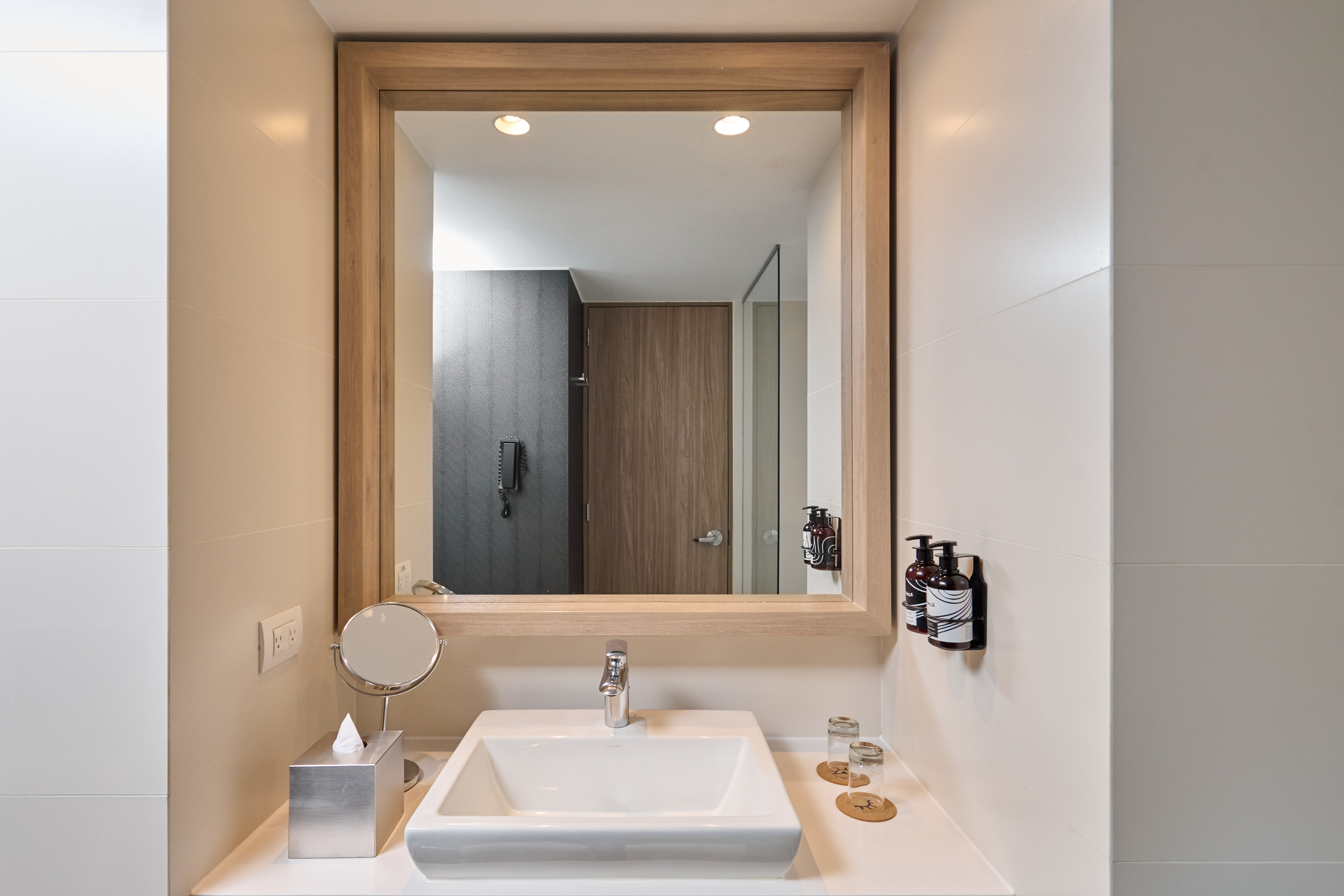 Contemporary hotel bathroom with white vanity, mirror, and essential toiletries.