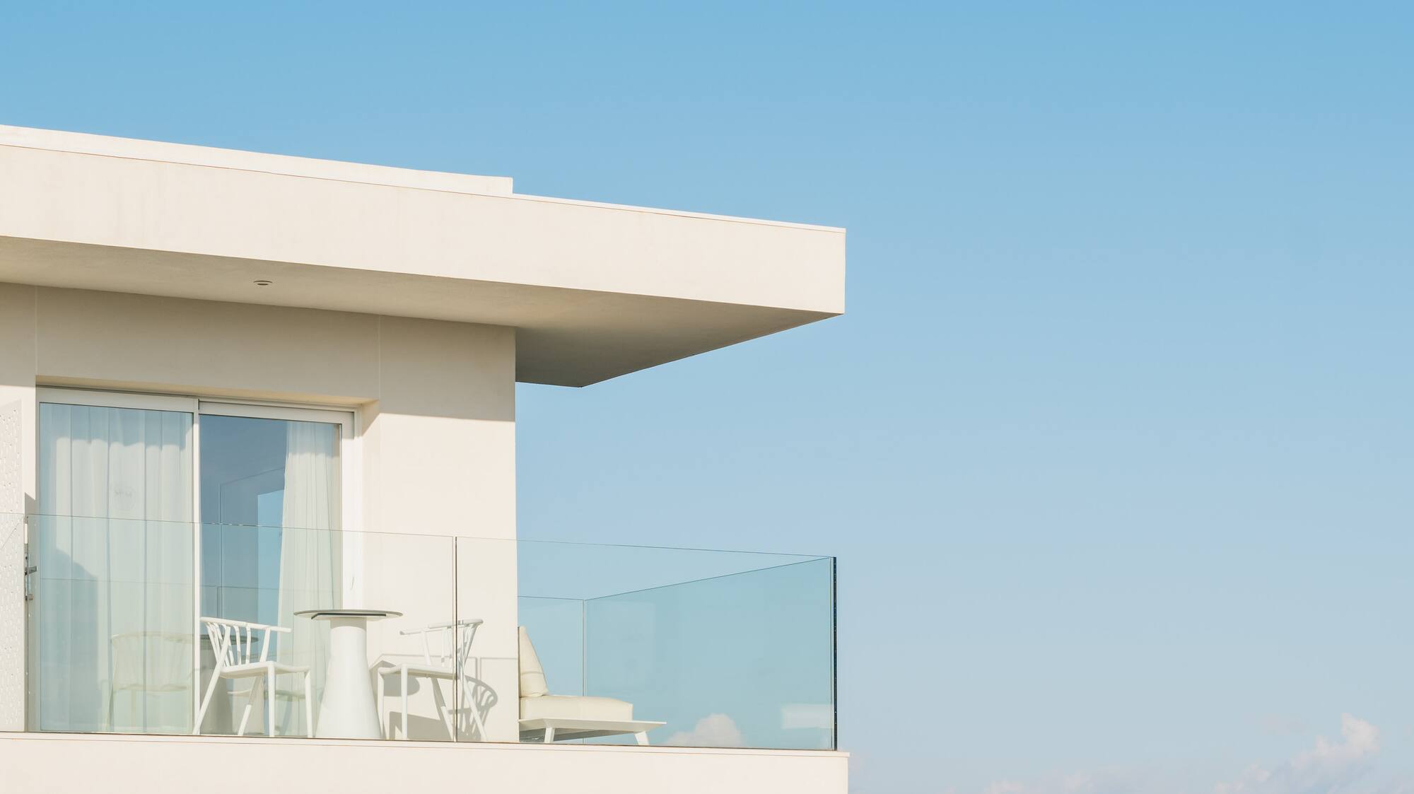 a white building with a glass balcony overlooking the ocean