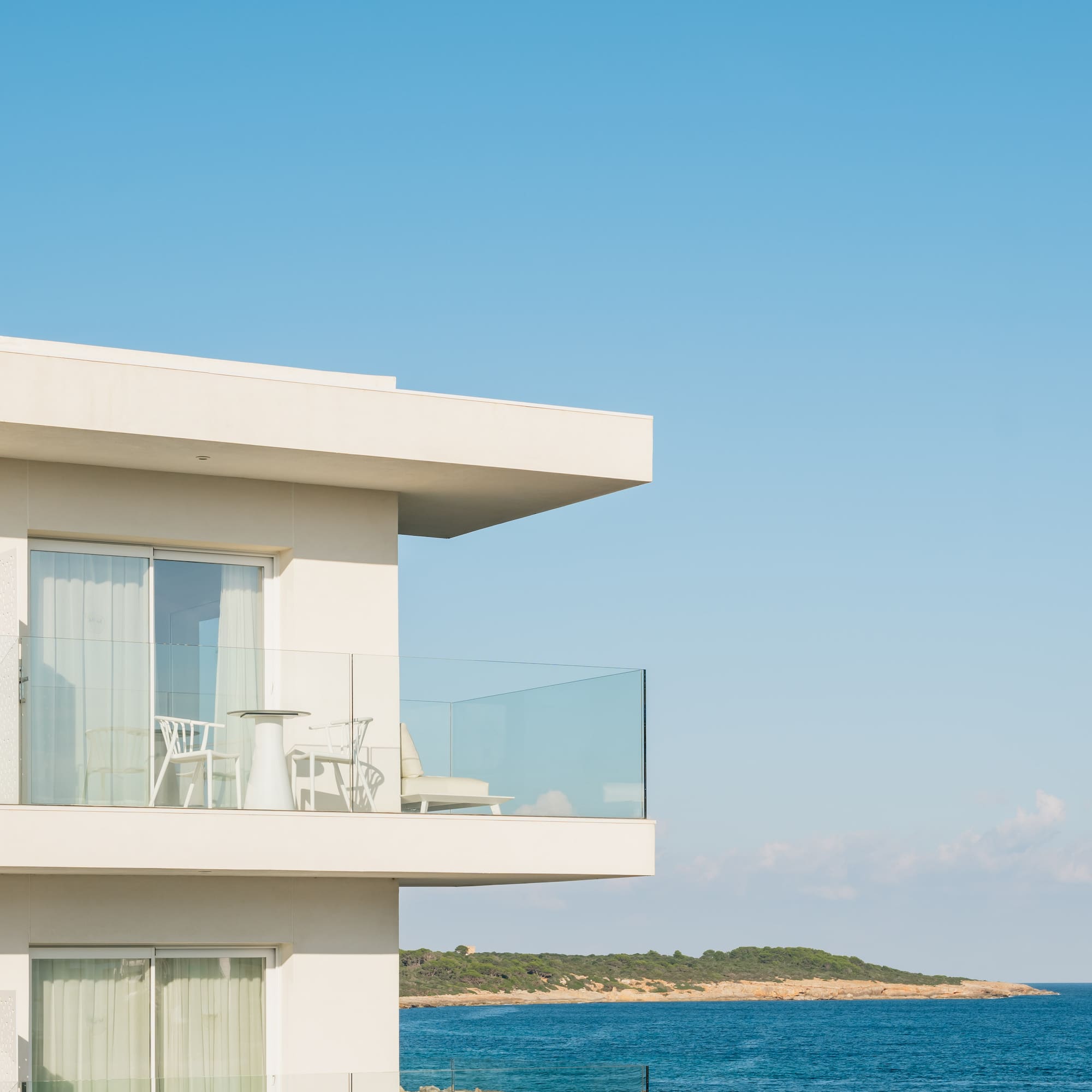 a white building with a glass balcony overlooking the ocean