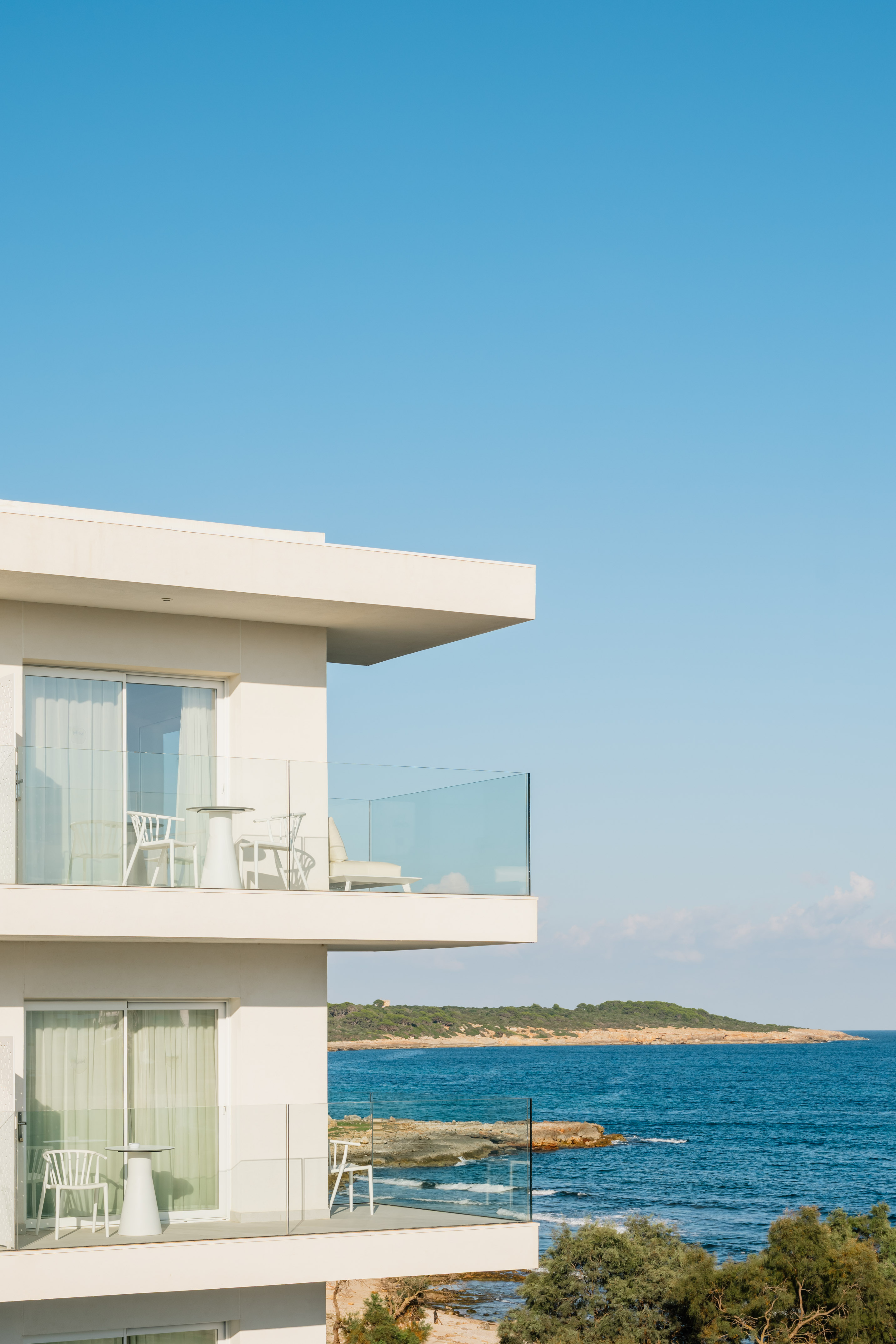 a white building with a glass balcony overlooking the ocean