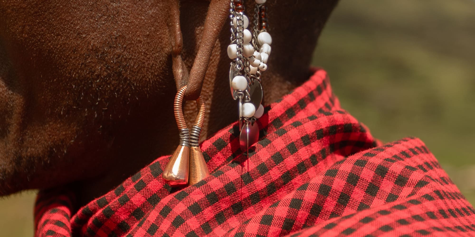 Maasai man's stretched ear with traditional beaded and copper earrings, red shuka.
