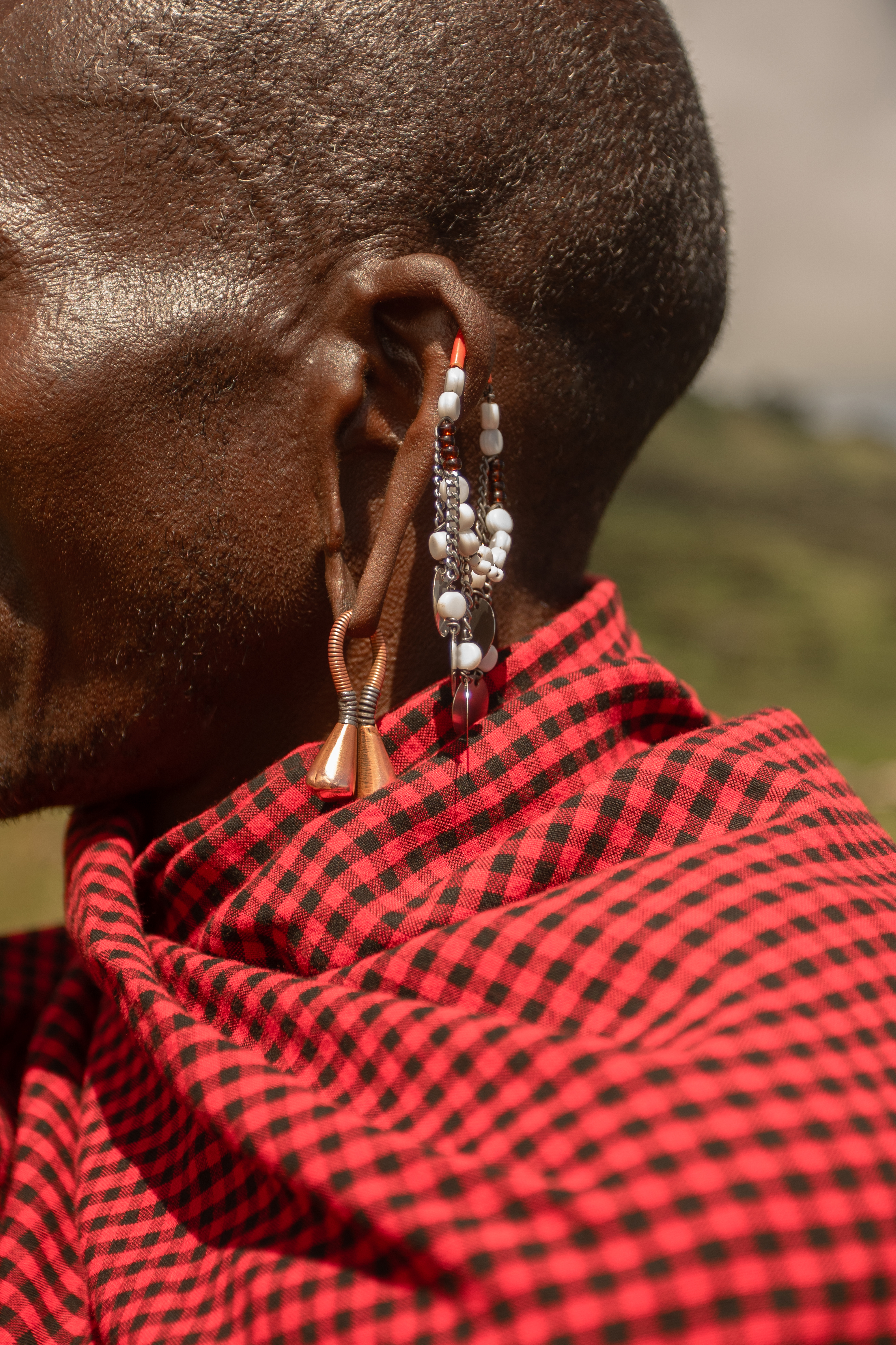 Maasai man's stretched ear with traditional beaded and copper earrings, red shuka.