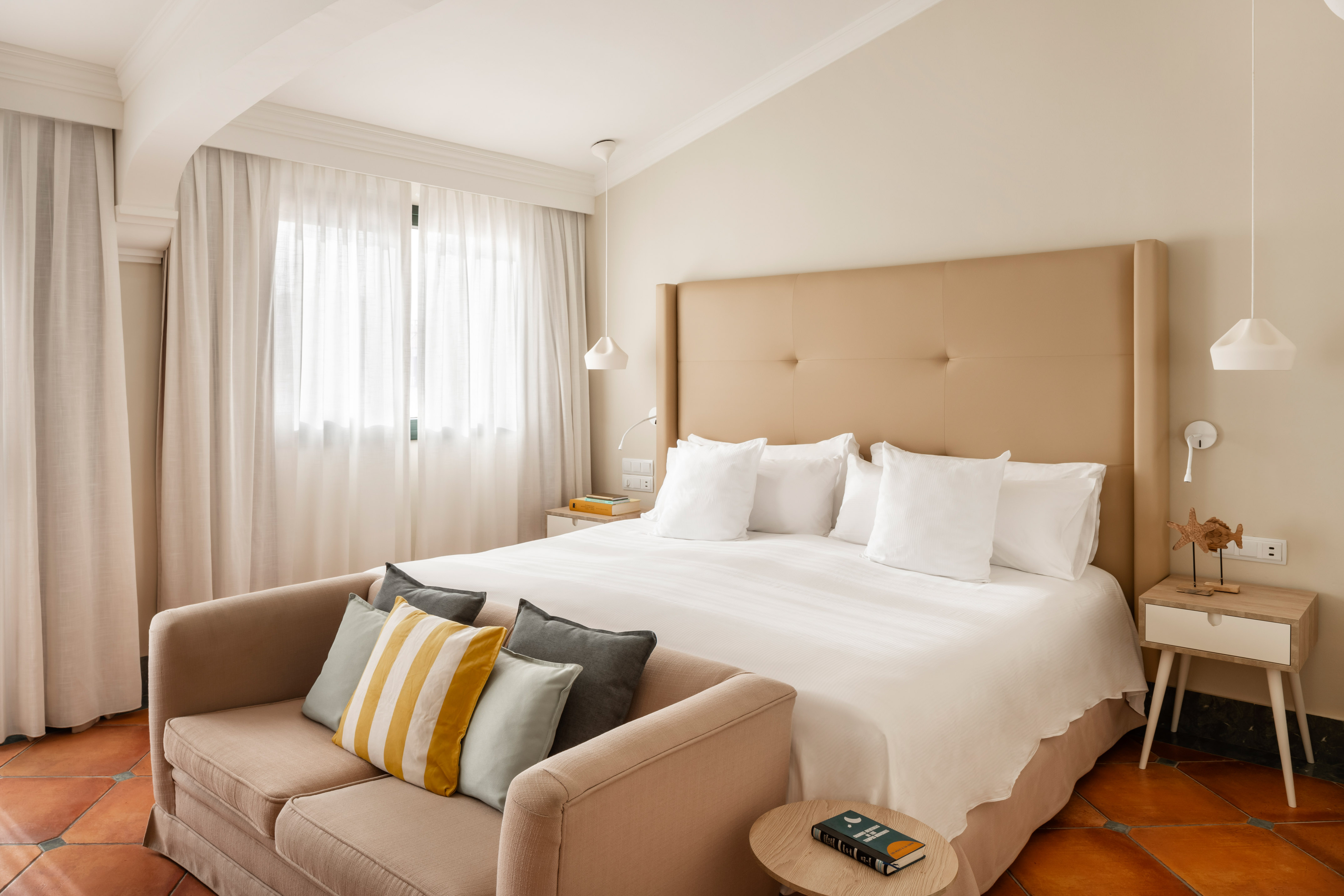 Bright modern hotel bedroom with large bed, sofa, and beige headboard.