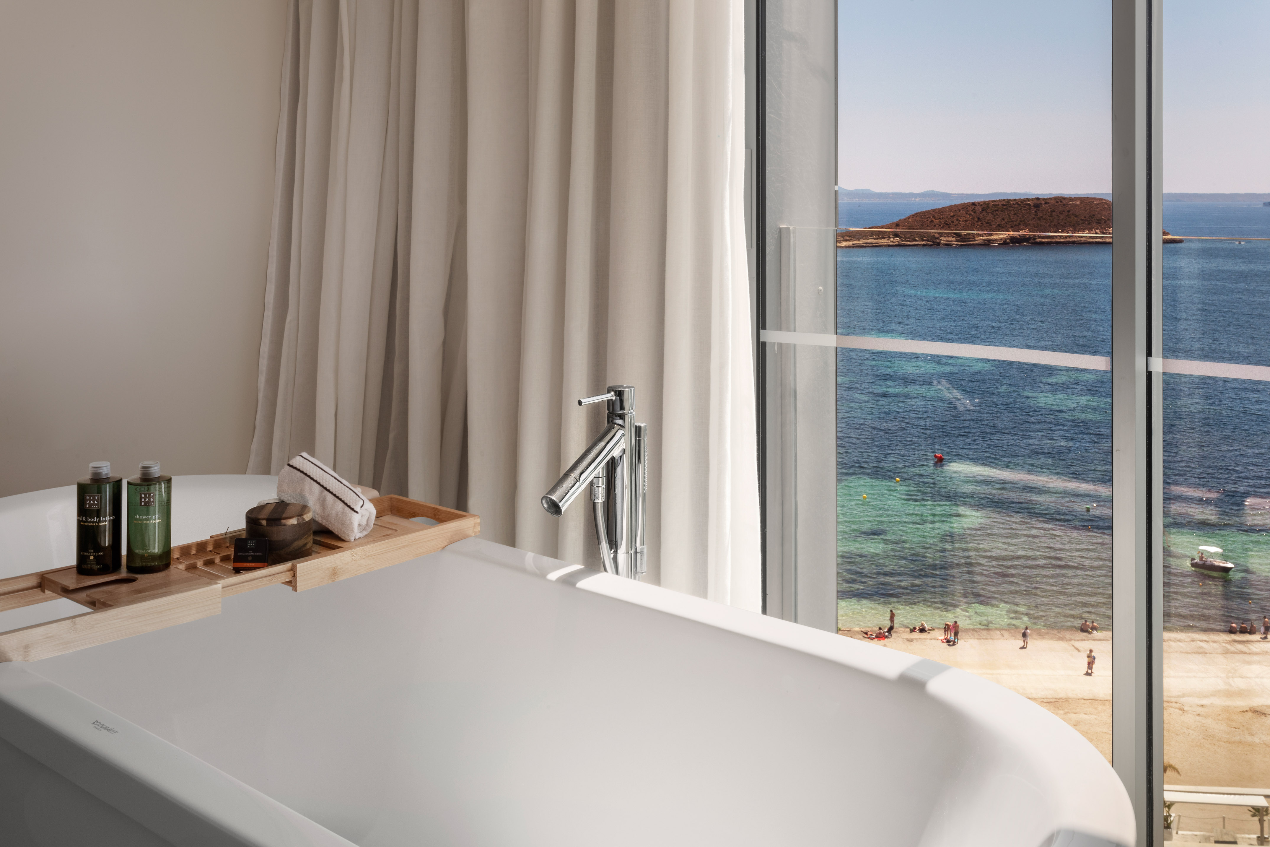 Luxury bathtub with bath caddy, overlooking a sunny beach and turquoise ocean.