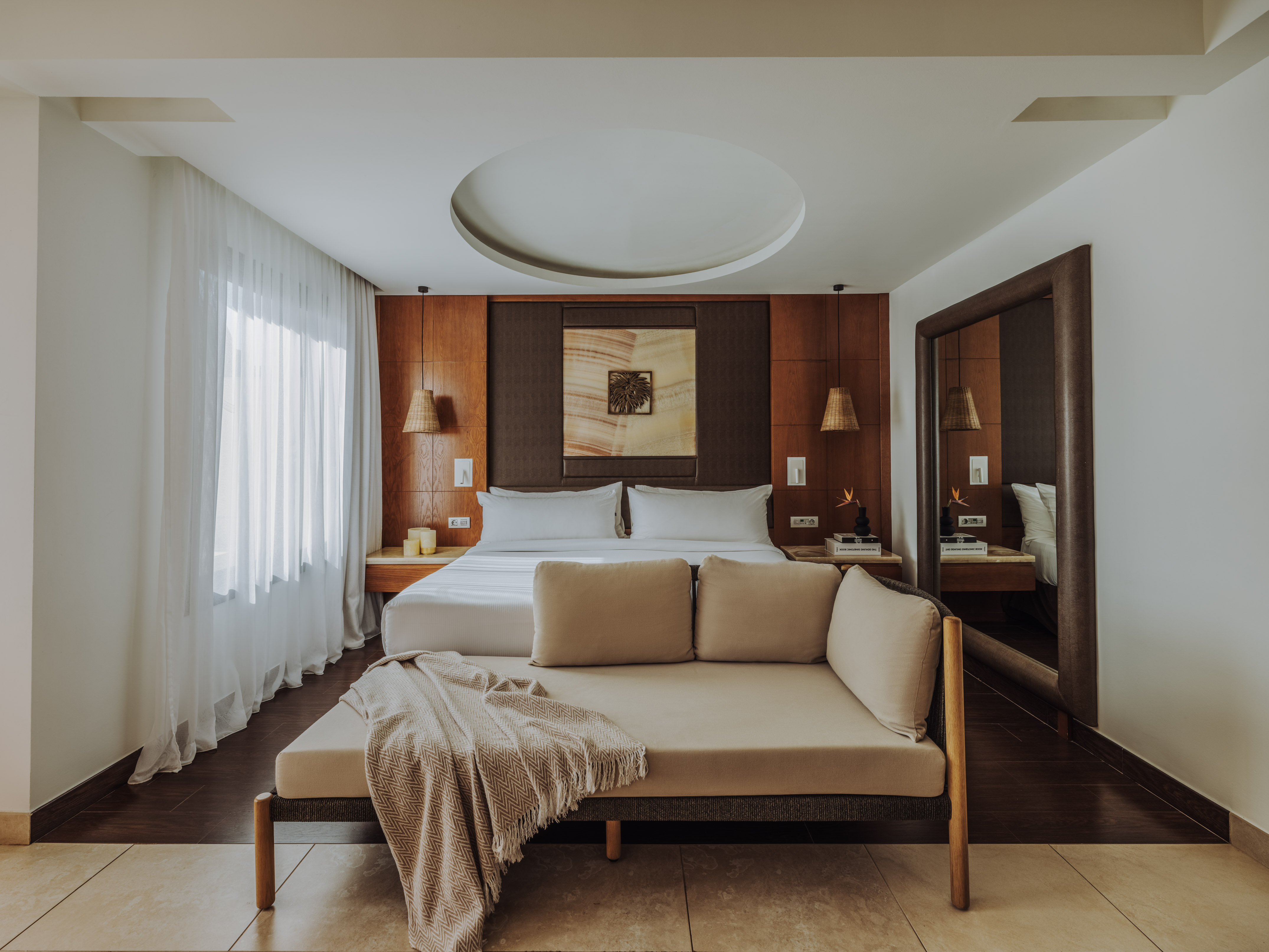 Modern bedroom with king bed, wooden headboard, sheer curtains, and chaise lounge.