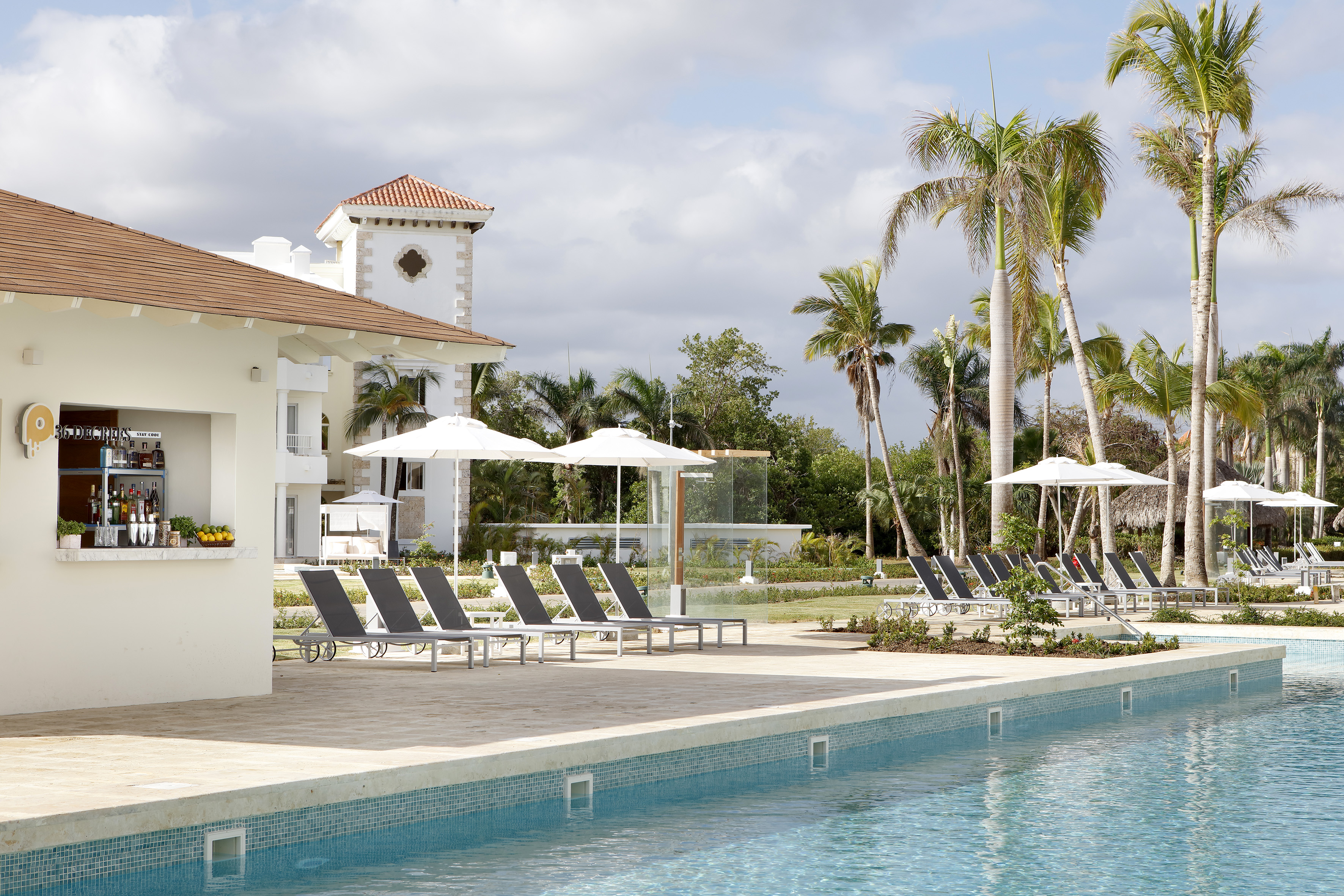 Resort swimming pool with lounge chairs, palm trees, and a poolside bar.