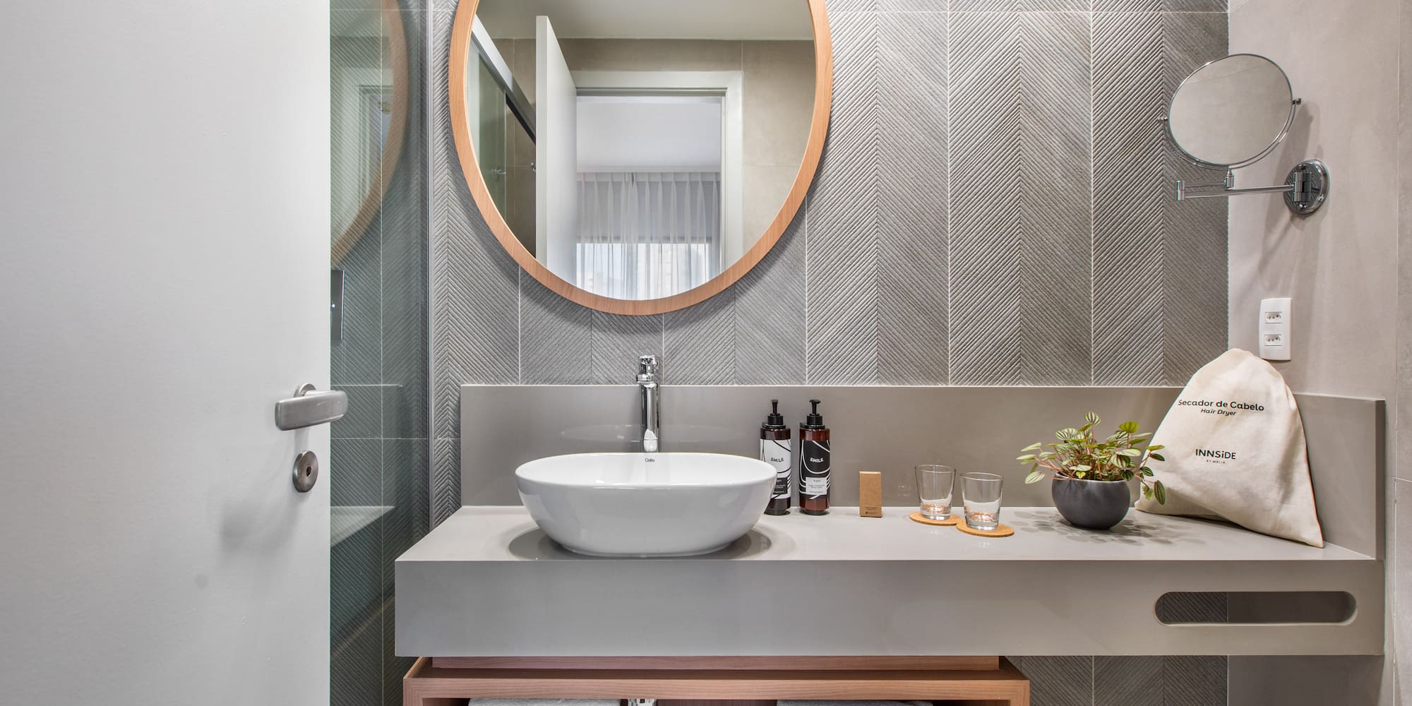 Modern hotel bathroom vanity with wood mirror, vessel sink, gray chevron tiles.